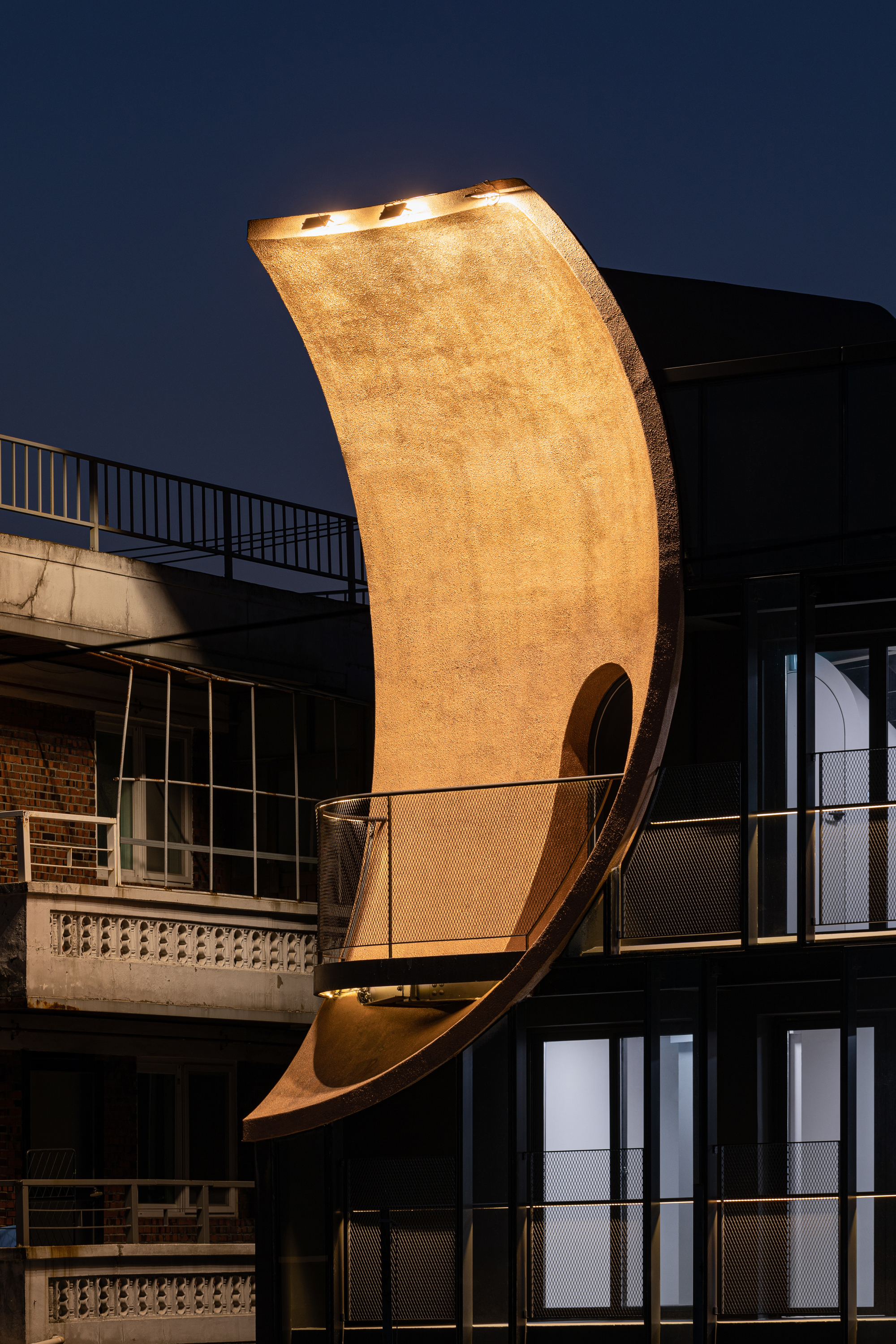 Night view of the illuminated curved timber element cantilevering from the building volume