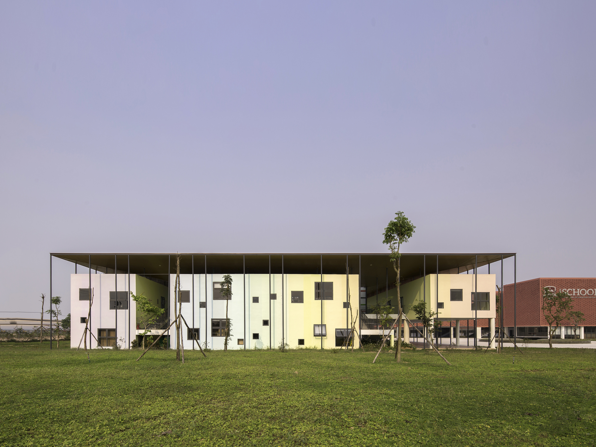 Long facade with thin roof overhang sheltering glass and panel volumes across a lawn
