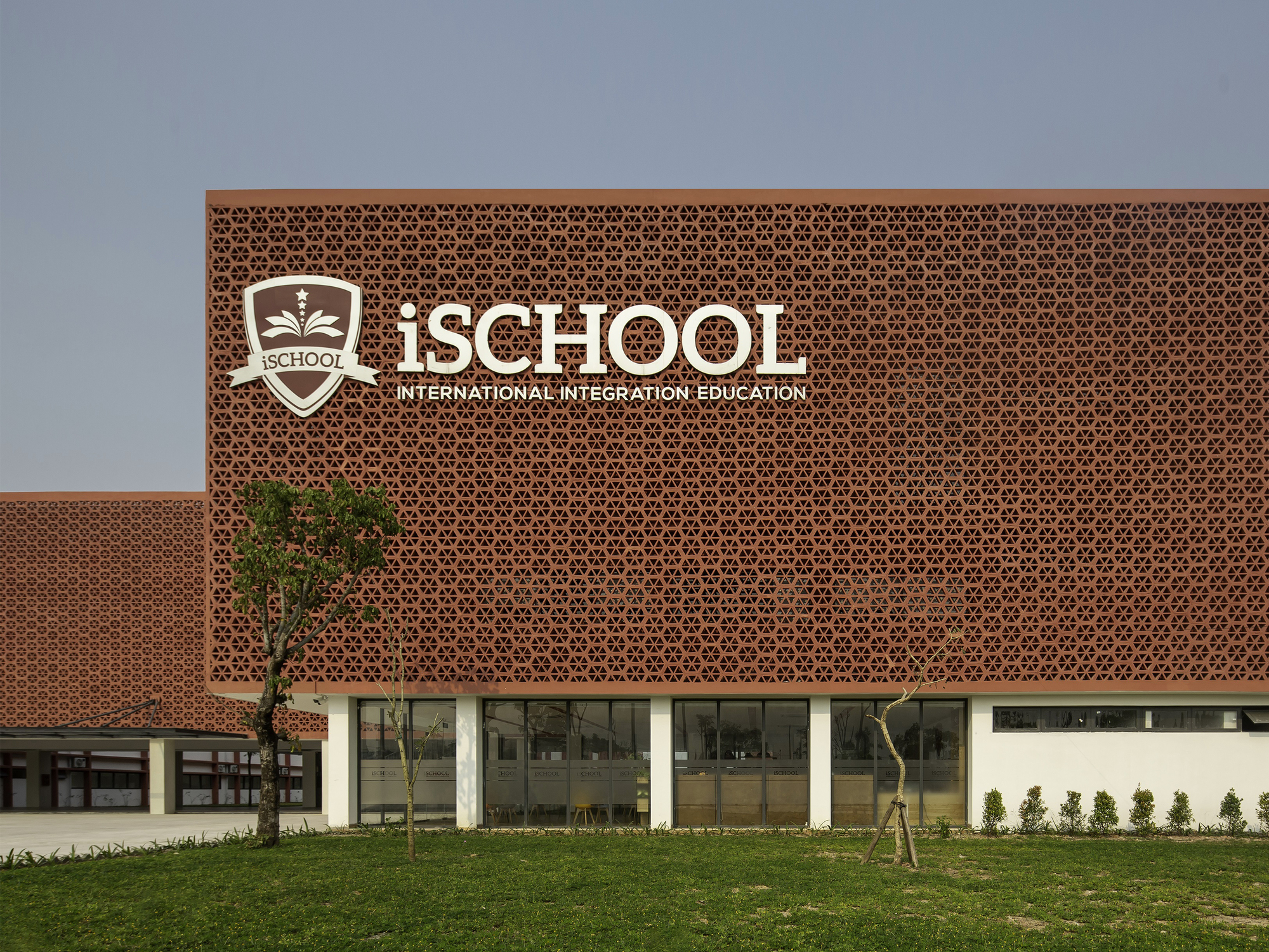 Perforated terracotta screen wall above glazed ground floor with young trees planted in front