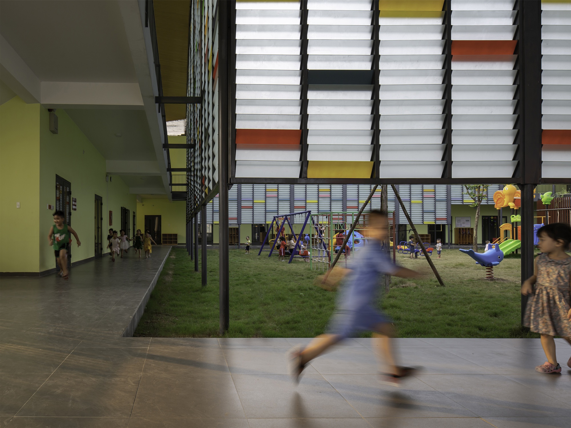 Covered courtyard with playground equipment and children in motion between classroom corridors