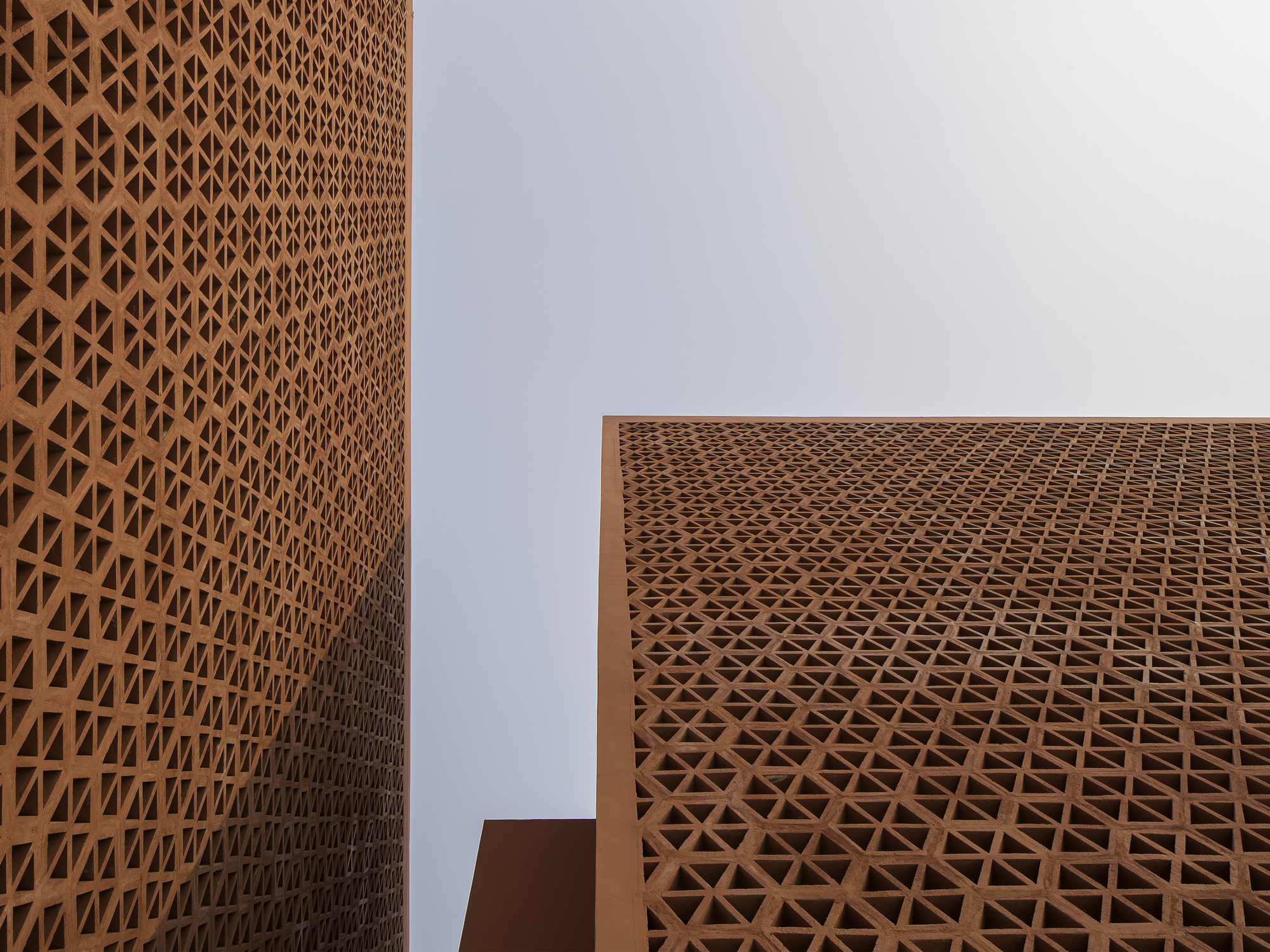 Upward view of geometric terracotta lattice panels wrapping two walls at a corner