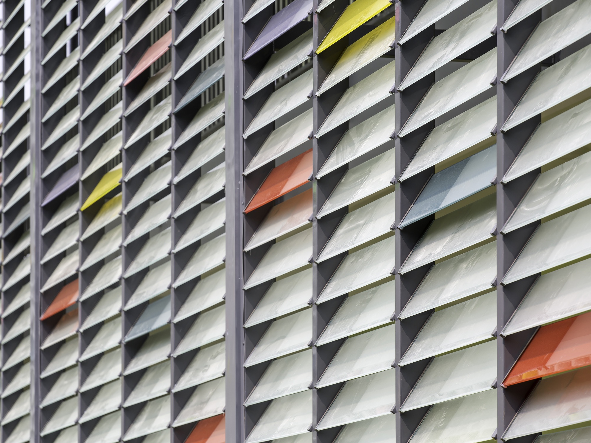 Close-up of angled metal louver facade with white fins accented by scattered yellow and orange blades
