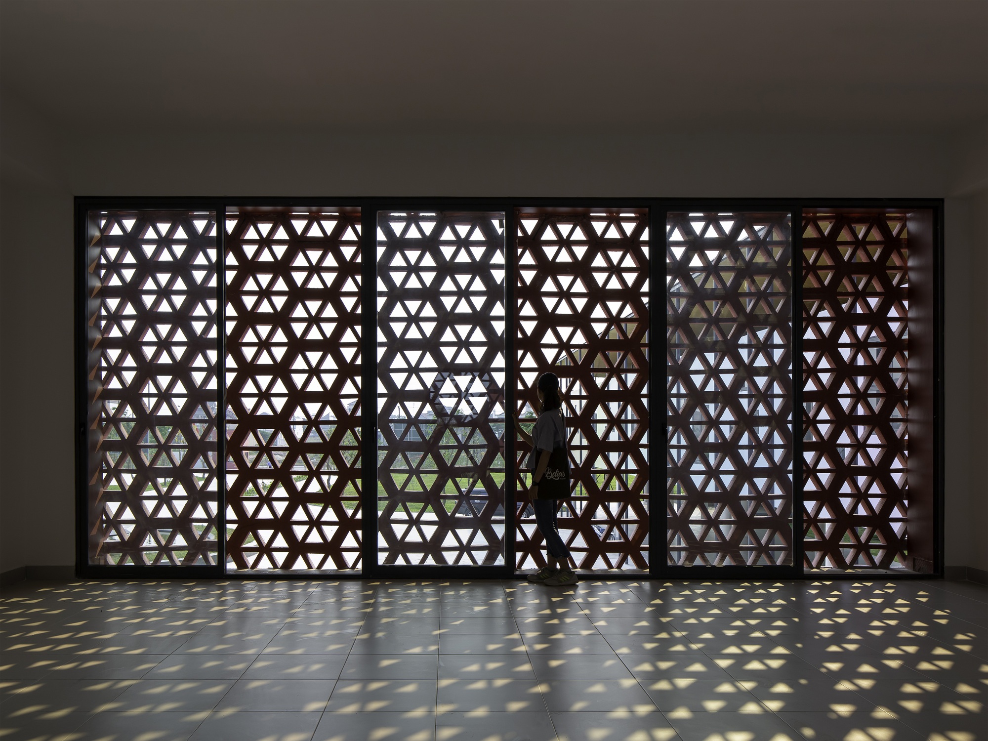 Interior corridor with triangular patterned screen wall casting dappled sunlight on polished floor