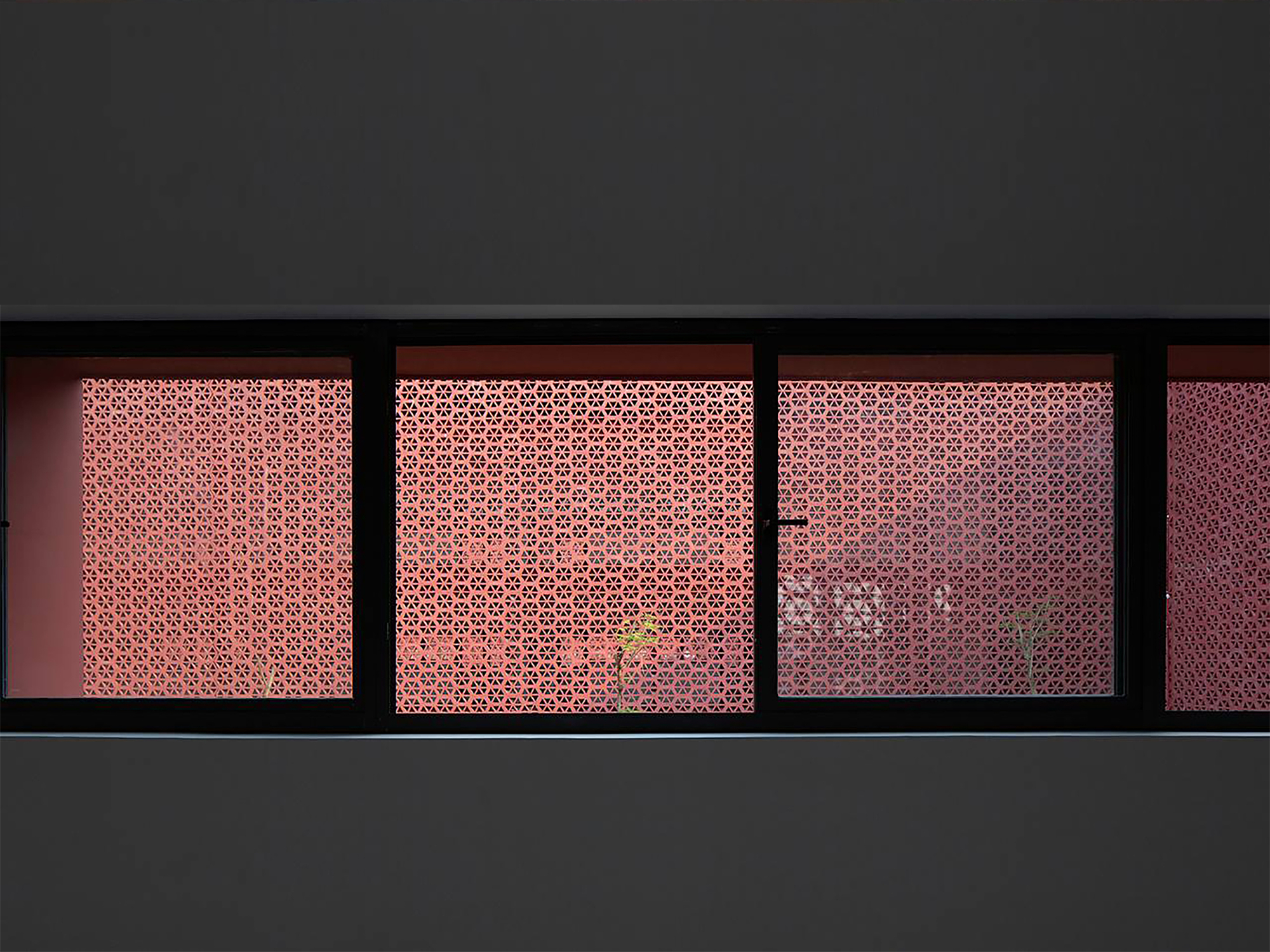 Horizontal strip windows with backlit geometric perforated screens in coral pink tones at dusk