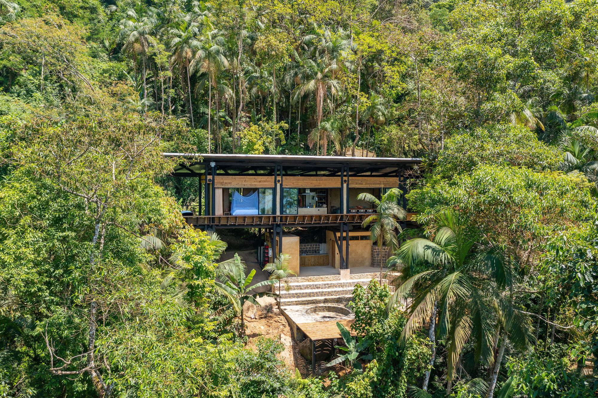Two-story timber structure with flat roof nestled into dense tropical vegetation on a sloped site