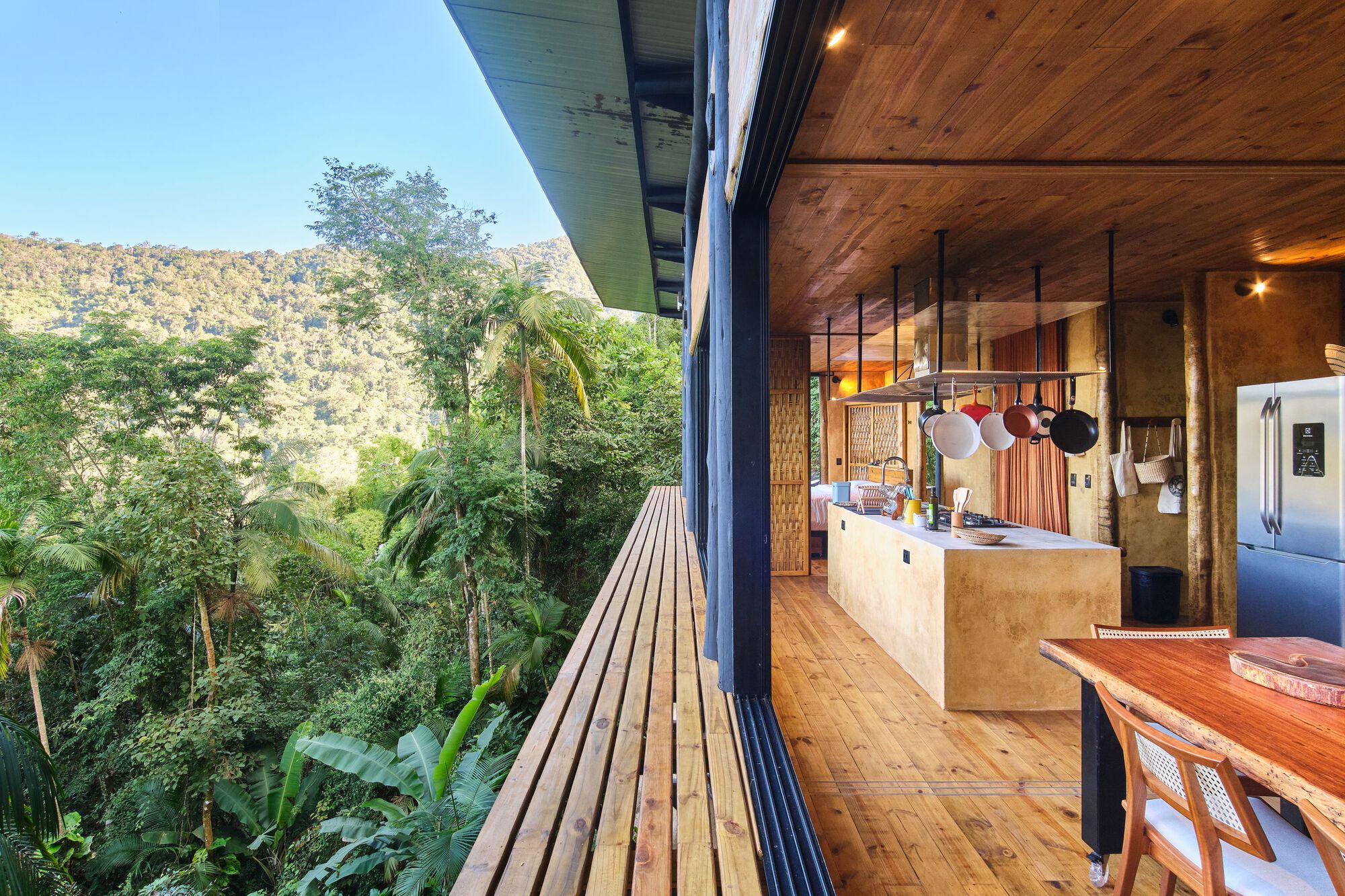 Open-plan kitchen and dining space with timber ceiling and slatted exterior deck overlooking forest