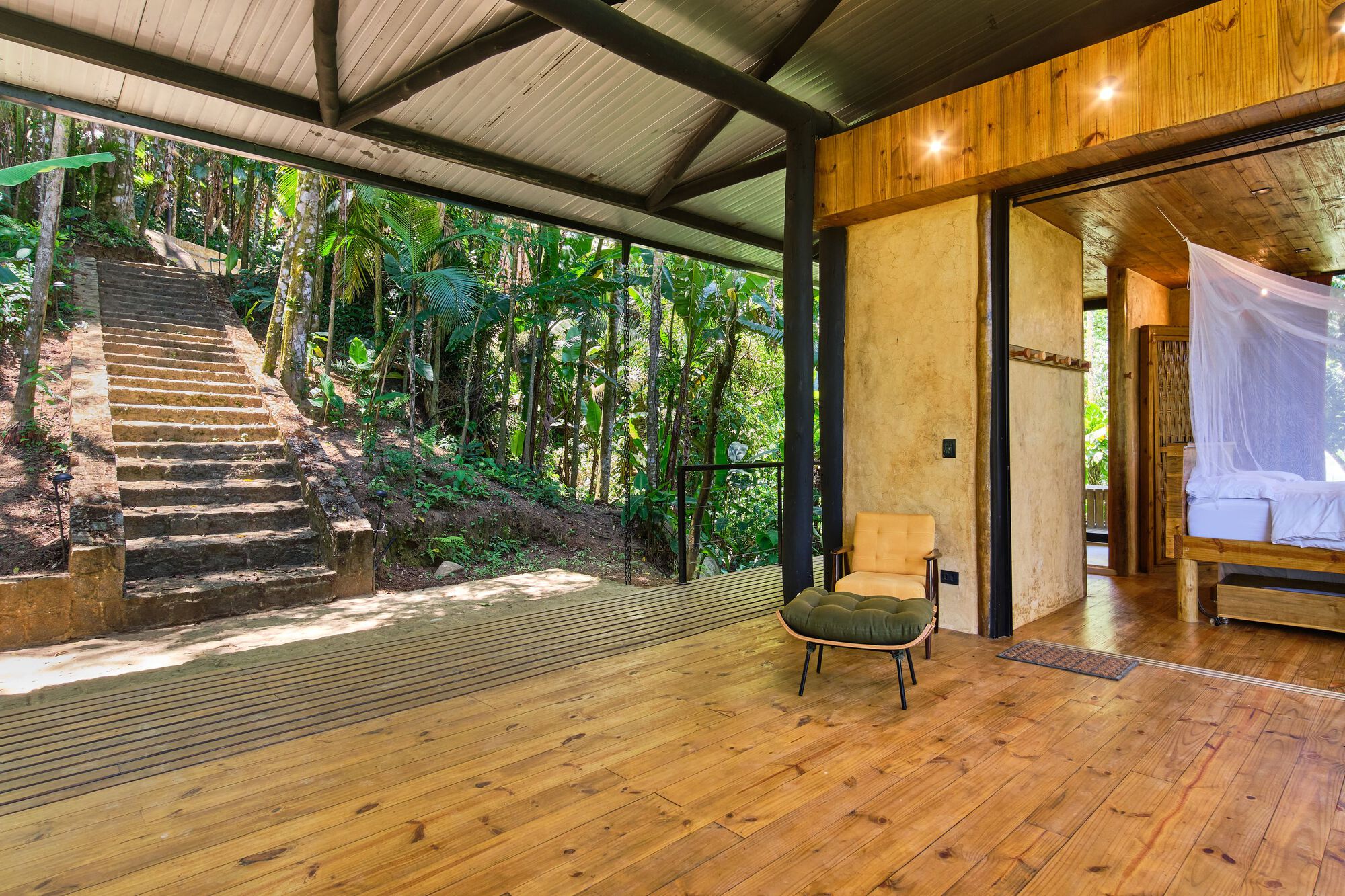 Open-air terrace with timber flooring and exposed steel beams looking toward exterior stairs cutting through the hillside