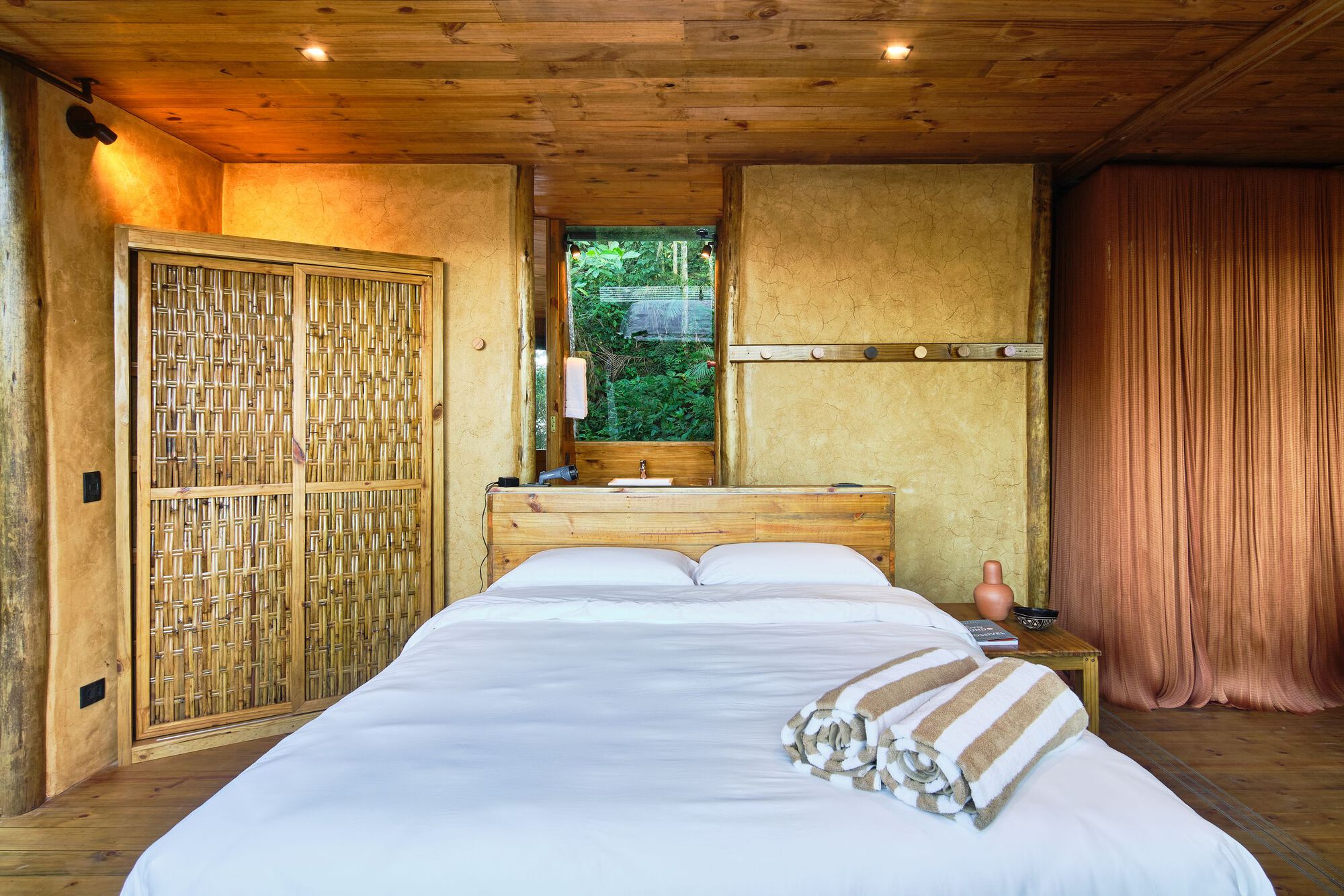 Bedroom interior with woven bamboo sliding doors and rammed earth wall beneath timber plank ceiling