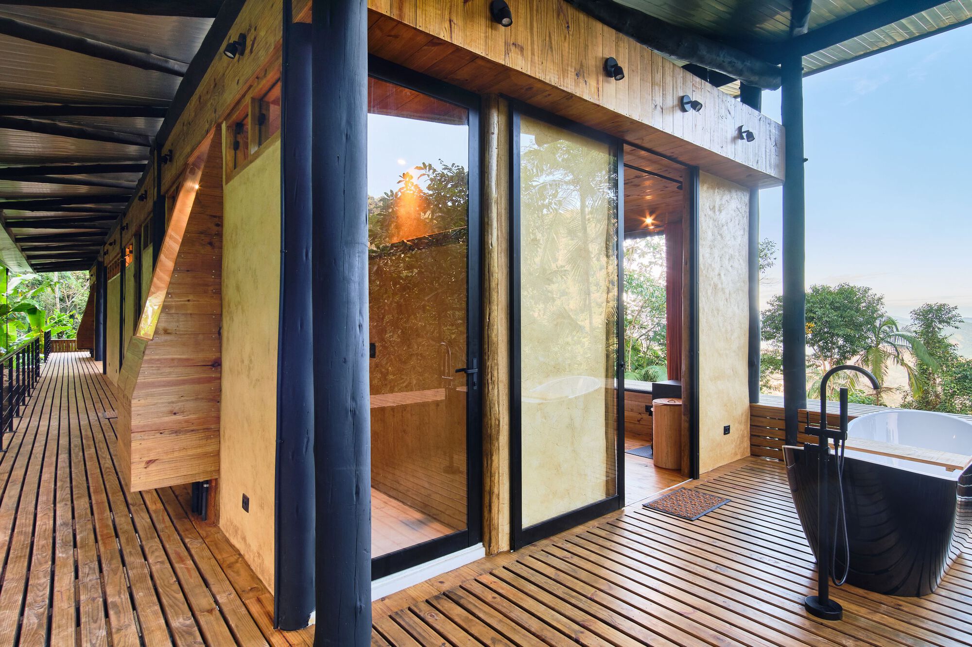 Exterior deck with freestanding bathtub and glazed bathroom enclosure beneath steel structure
