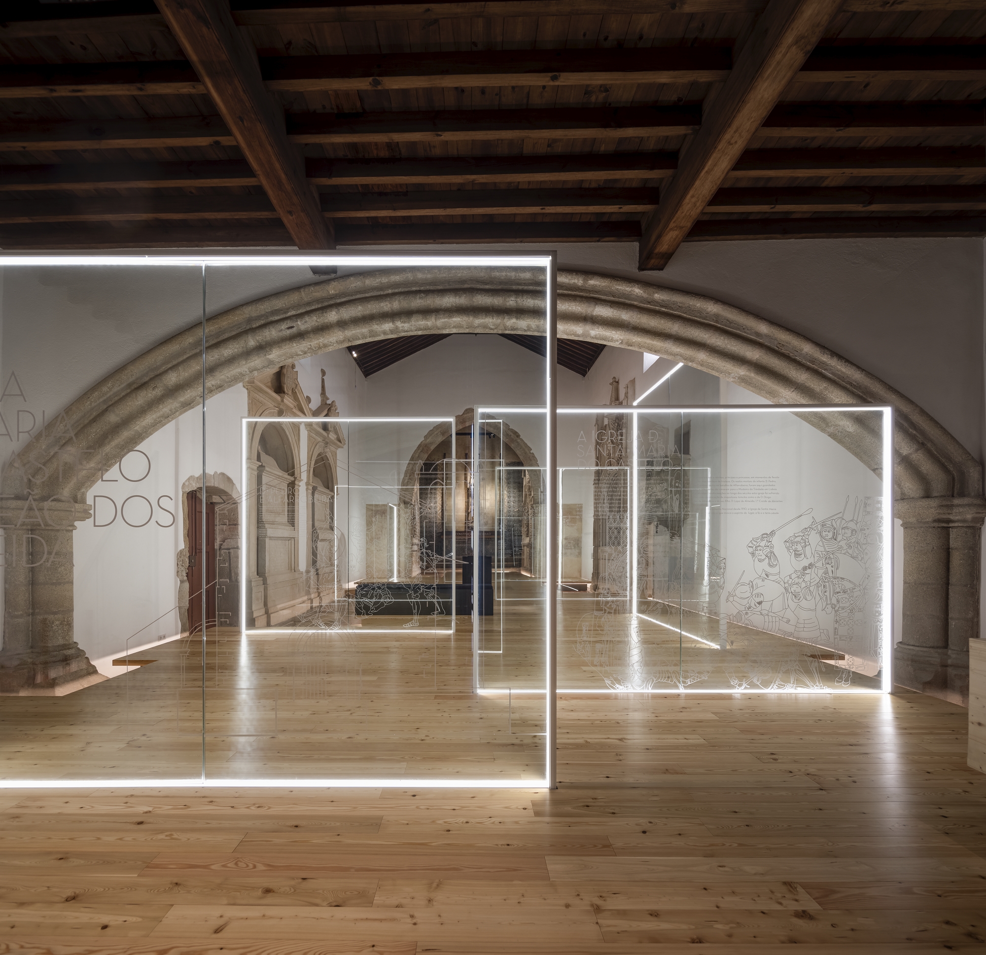 Illuminated glass panel installation beneath exposed timber beams in a vaulted gallery with stone arches
