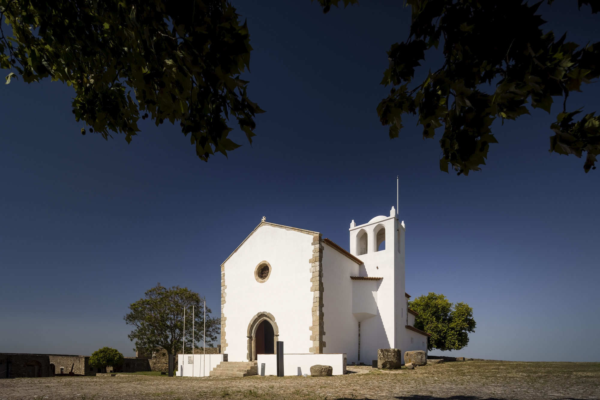 White plastered chapel with bell tower and stone portal on a hilltop under clear blue sky