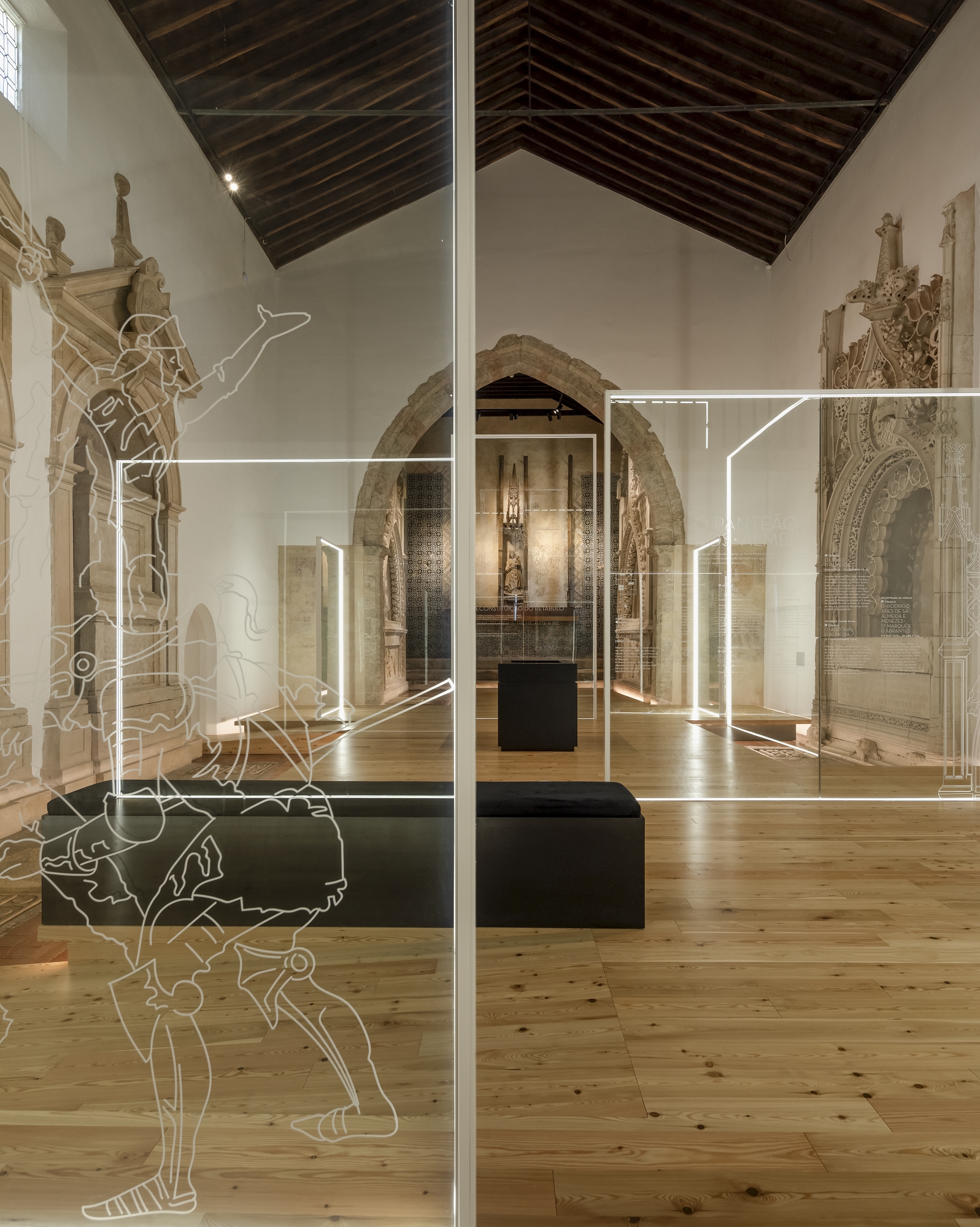 Glass partition with etched line drawings dividing a timber-floored nave with stone portals and rafters