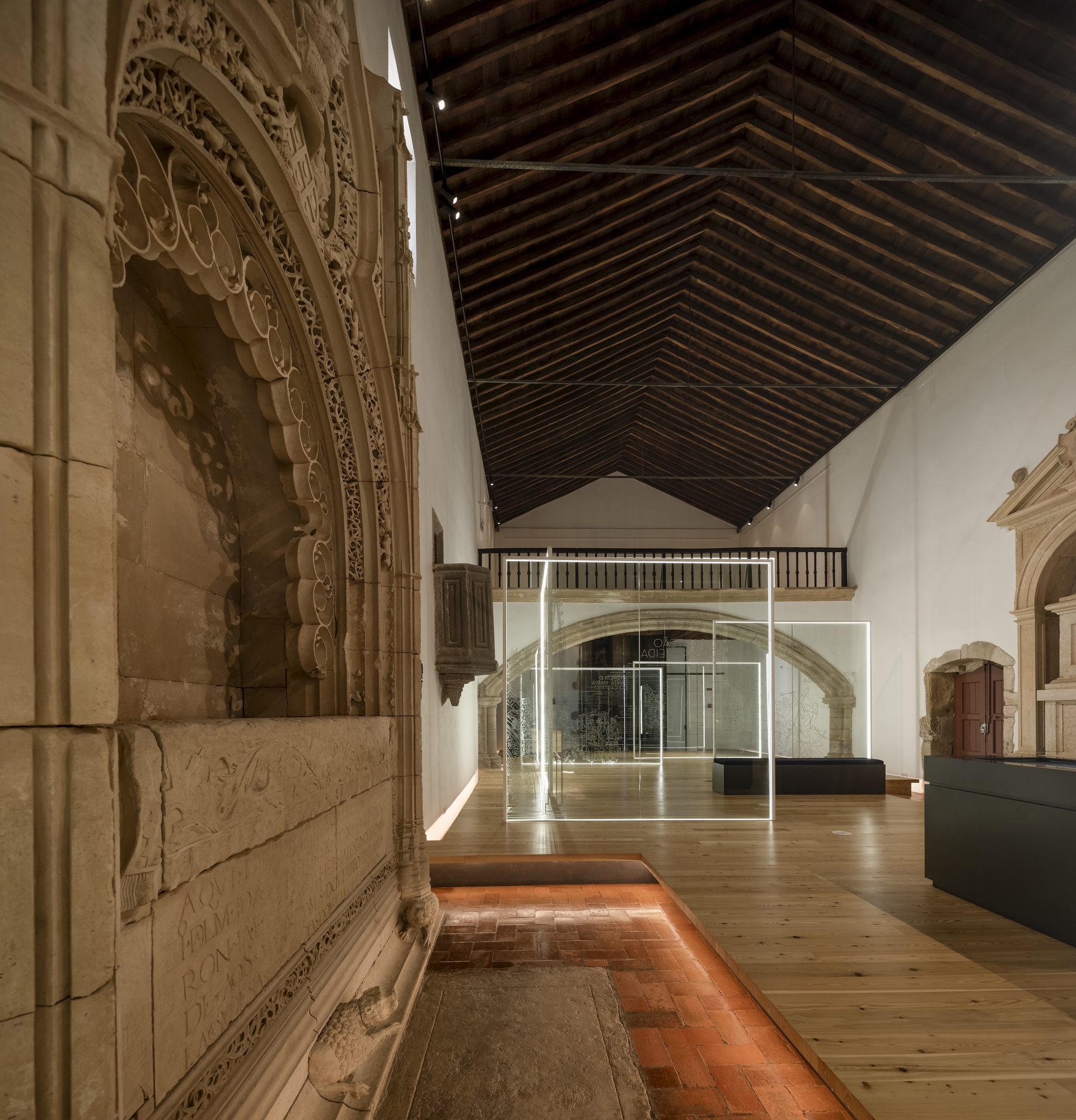 Gallery interior with carved stone portal, exposed timber ceiling and illuminated glass partitions on timber floor
