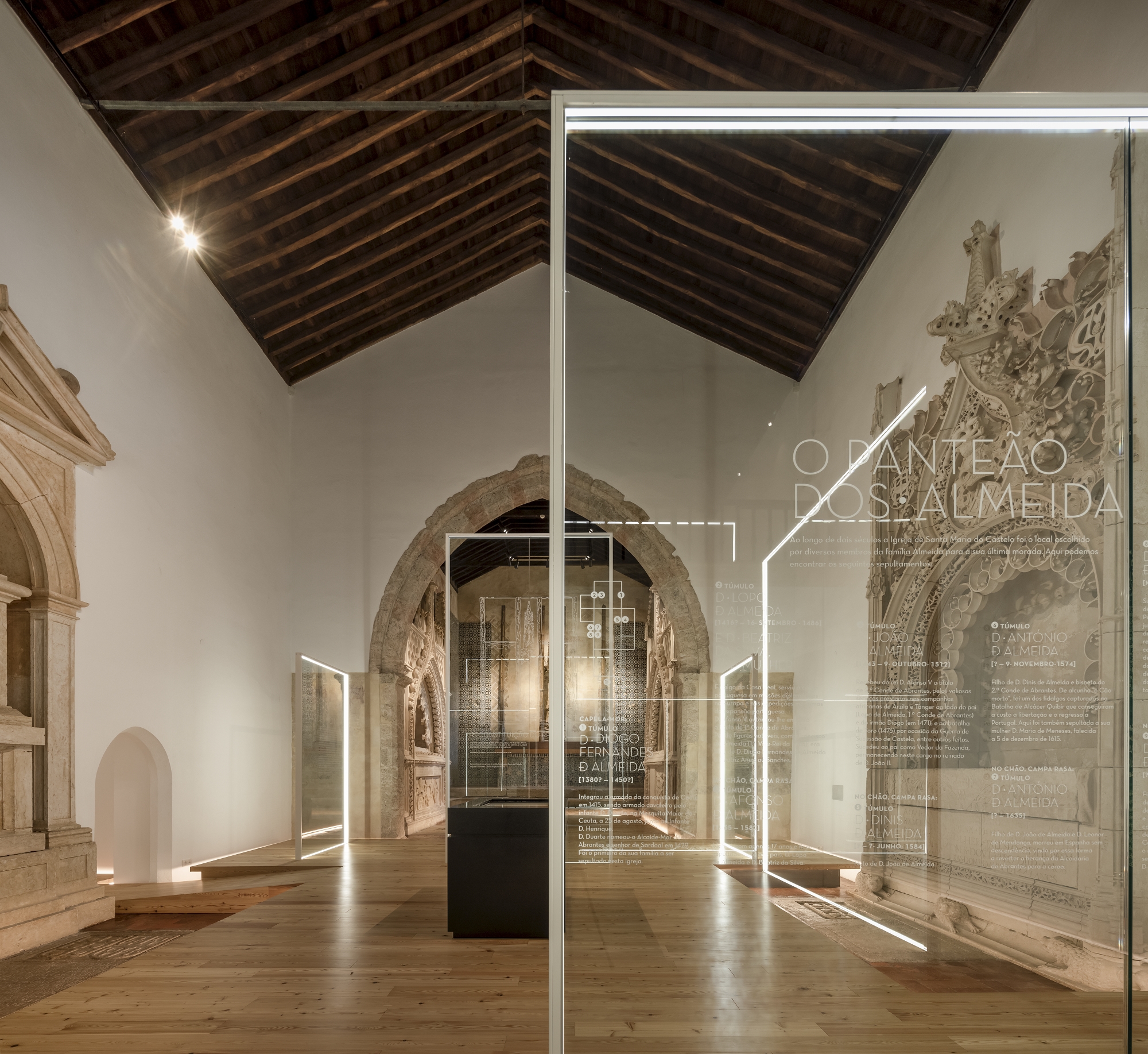 View through glass panels with etched text toward stone arches and dark timber ceiling beams