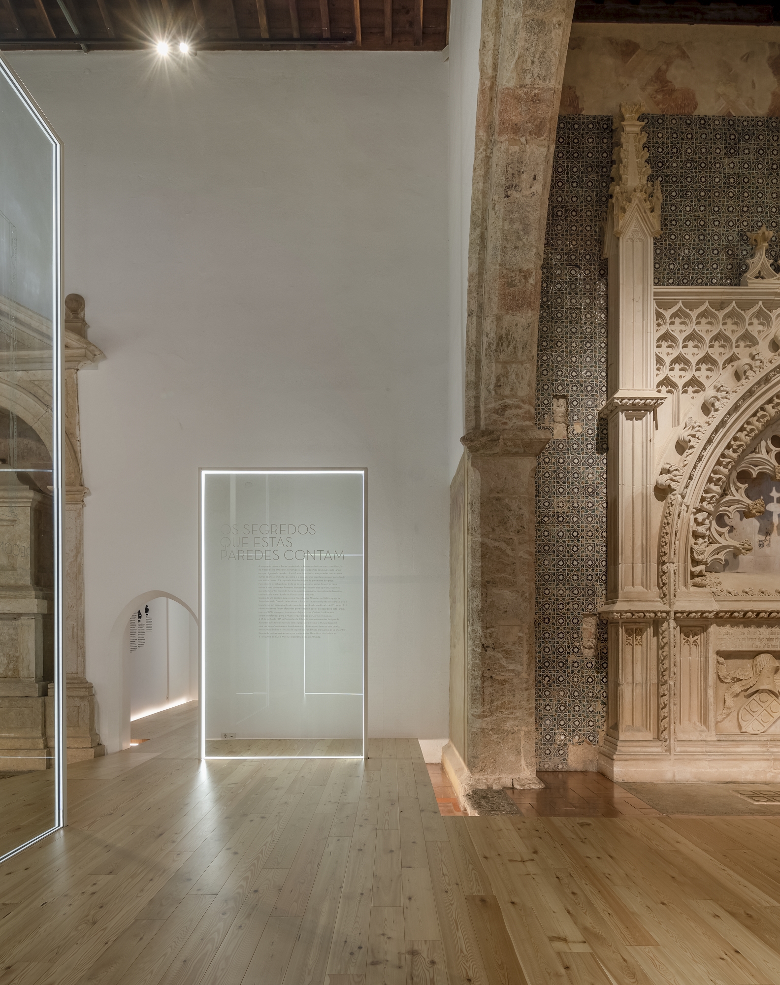 Backlit glass partition with etched inscription standing beside a weathered stone column and tiled wall