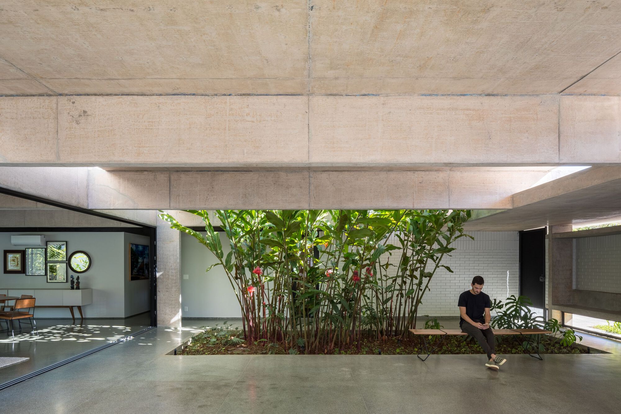 Interior courtyard planted bed with tropical foliage beneath board-formed concrete beams and a person seated