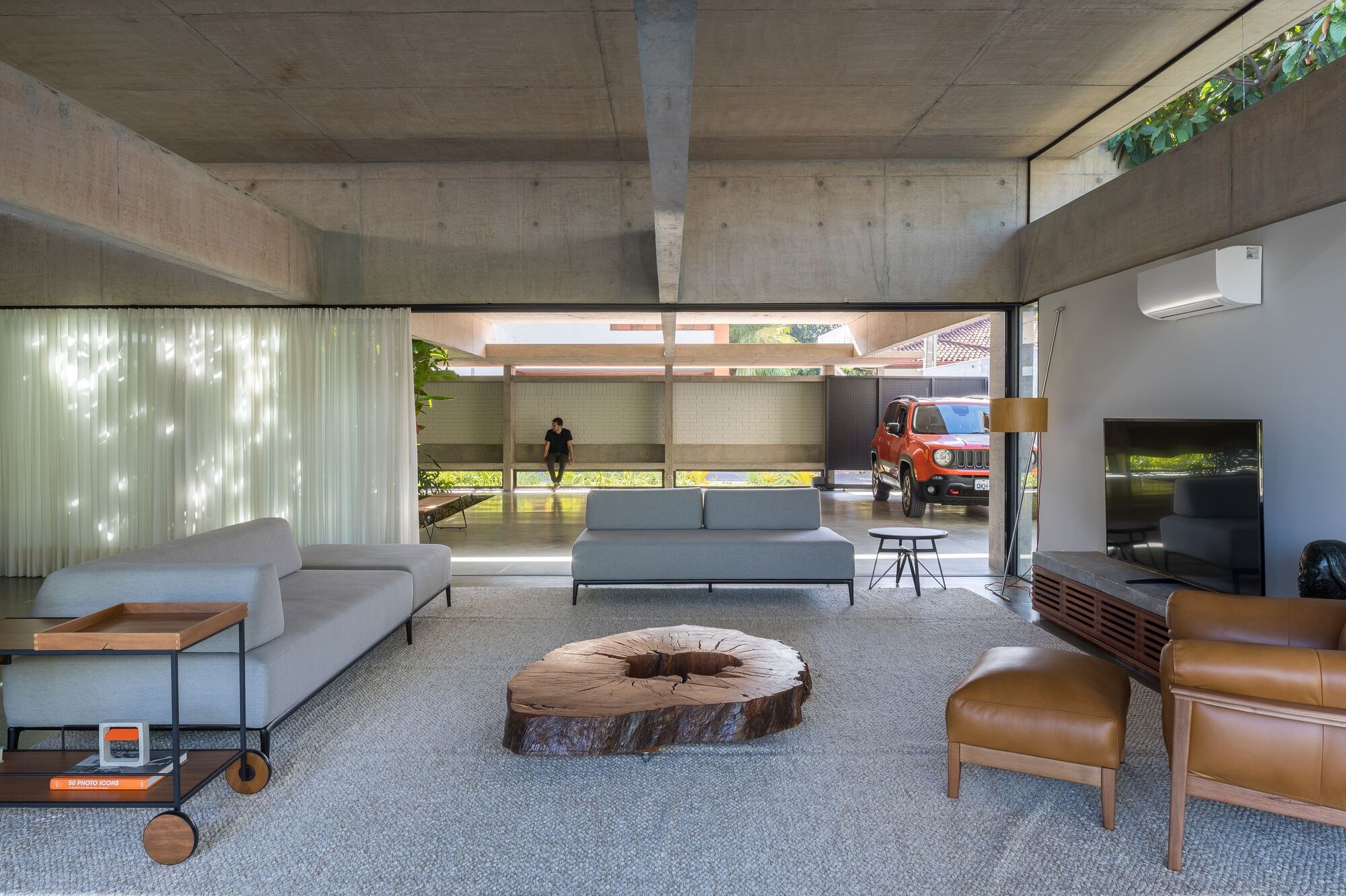 Living area with exposed concrete ceiling beams and clerestory windows filtering dappled sunlight onto the floor