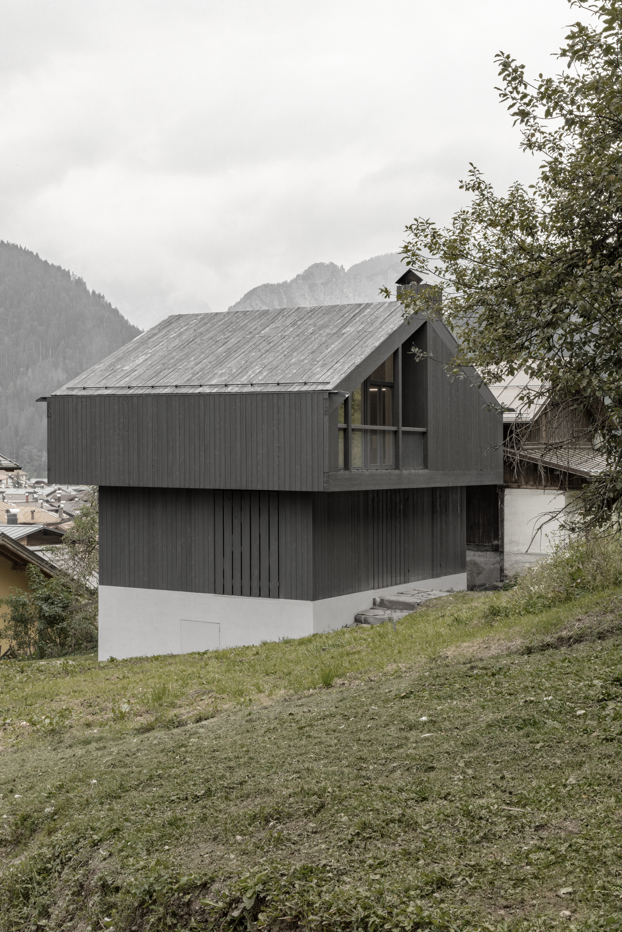 Corner view of dark timber facade with recessed upper balcony framed by deciduous trees