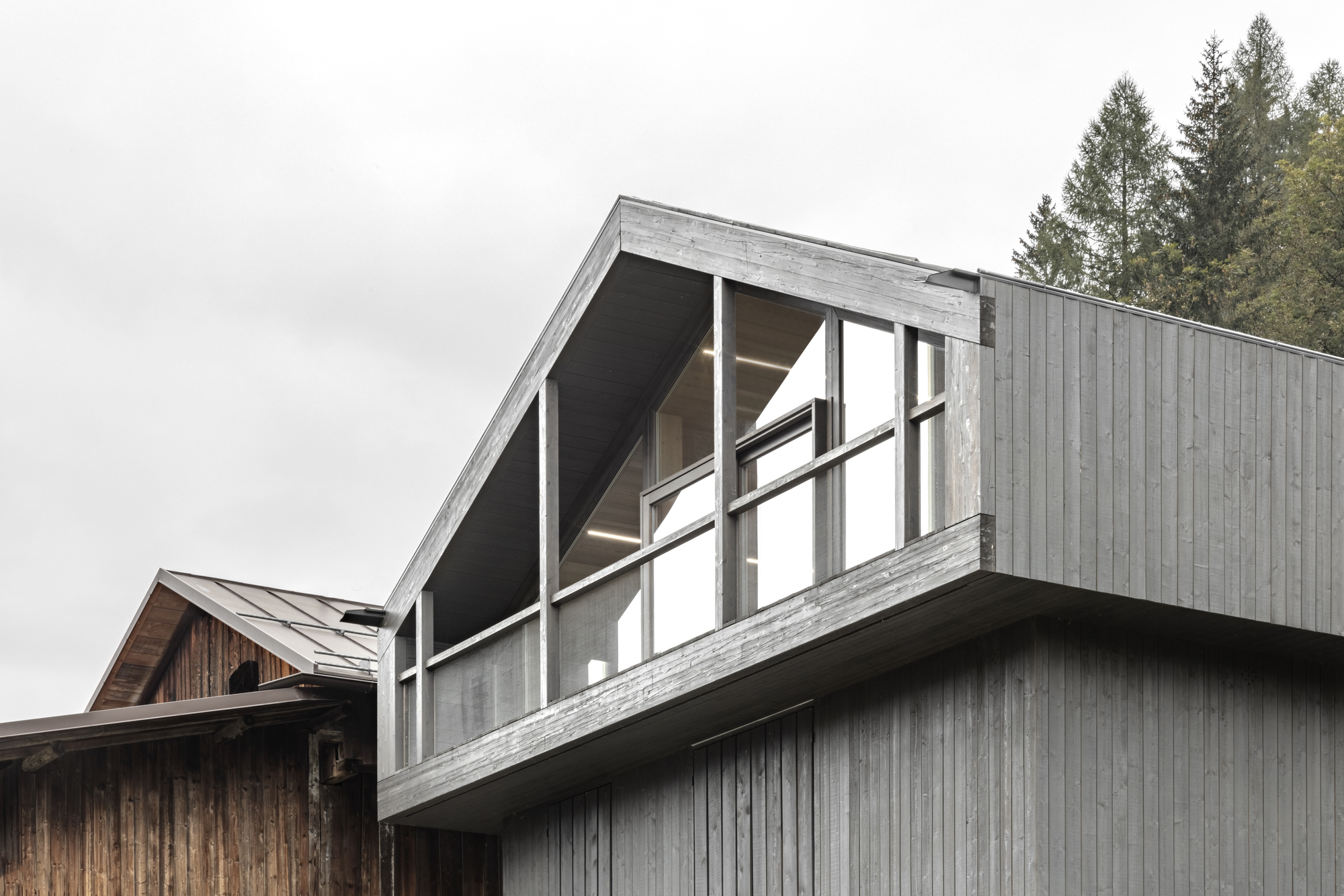 Vertical timber cladding and angled glazed section with exposed beams under an overcast sky