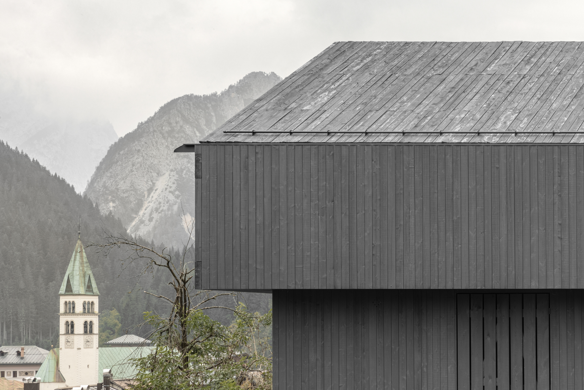 Weathered timber roof and dark wood facade with distant church tower visible through morning mist