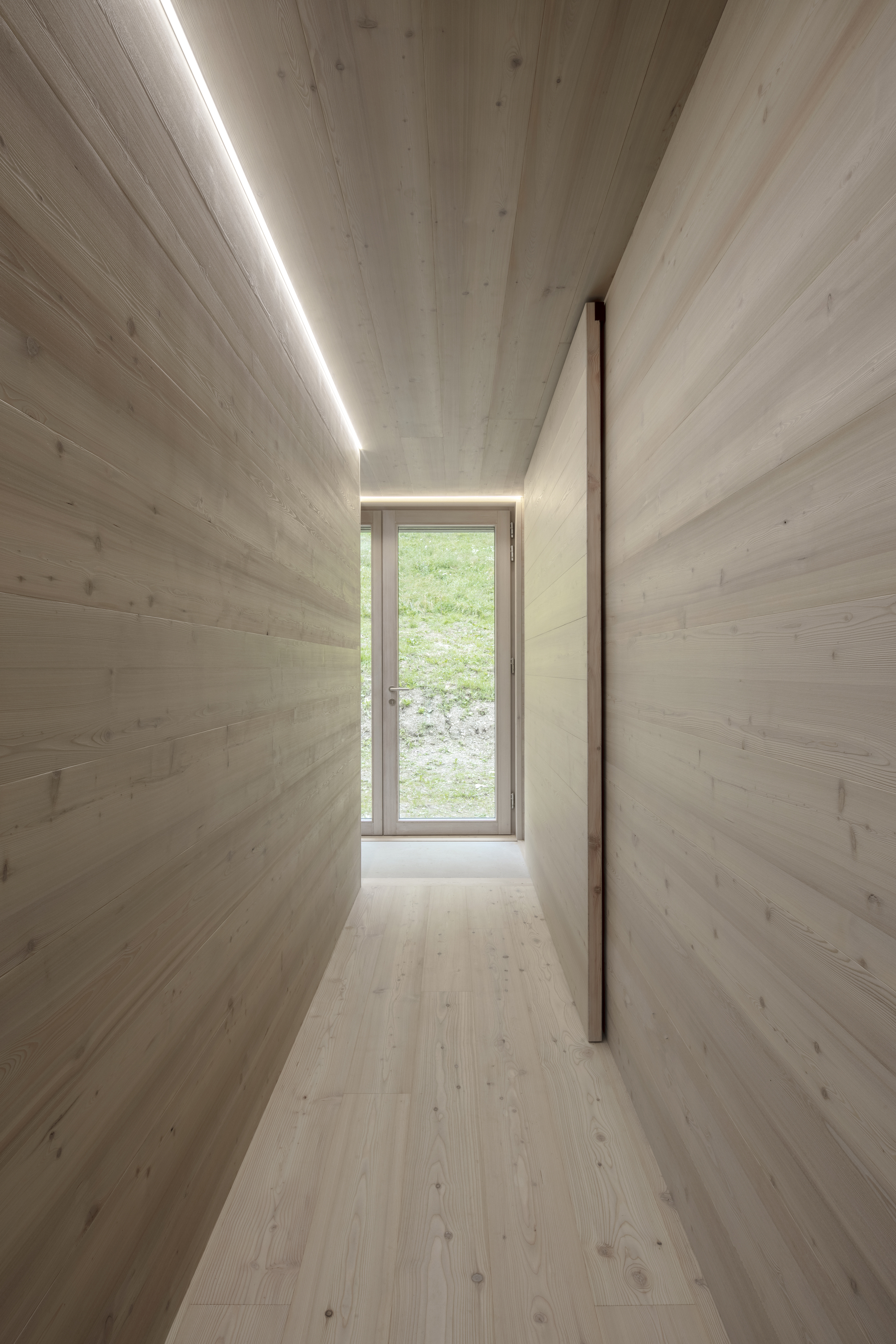 Narrow corridor with horizontal timber cladding and linear ceiling light leading to a glazed door