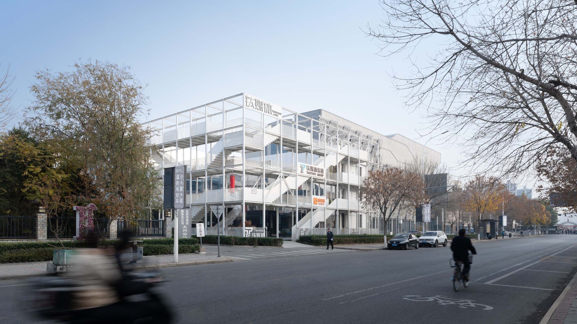 Street view of the white structural frame with cyclists and pedestrians passing in autumn