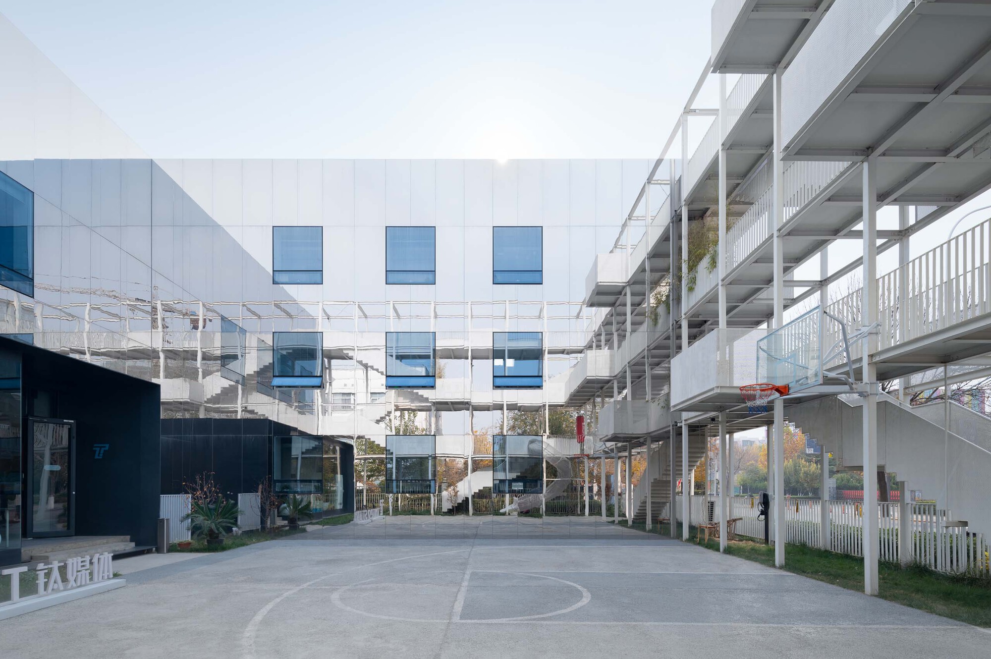 White panel facade with recessed blue windows flanked by open structural frame and planted courtyard below