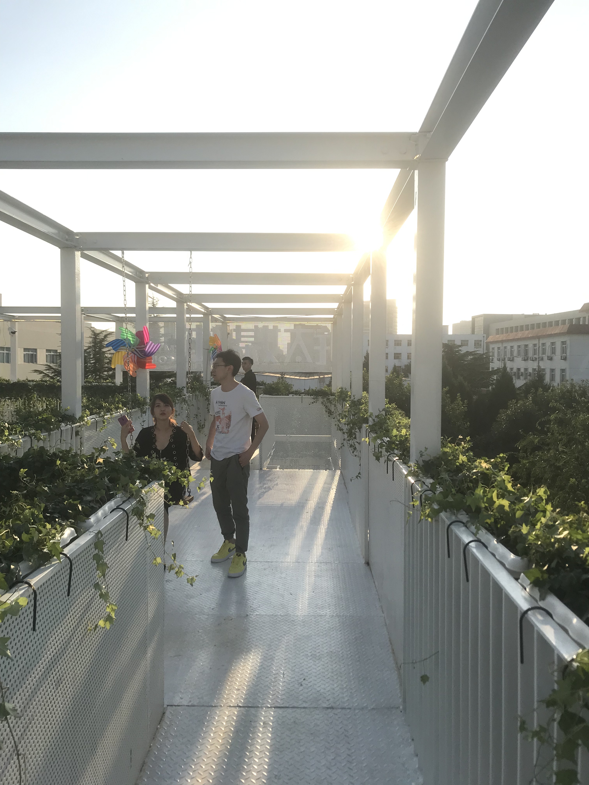 Rooftop pathway beneath white steel pergola with two figures walking at sunset