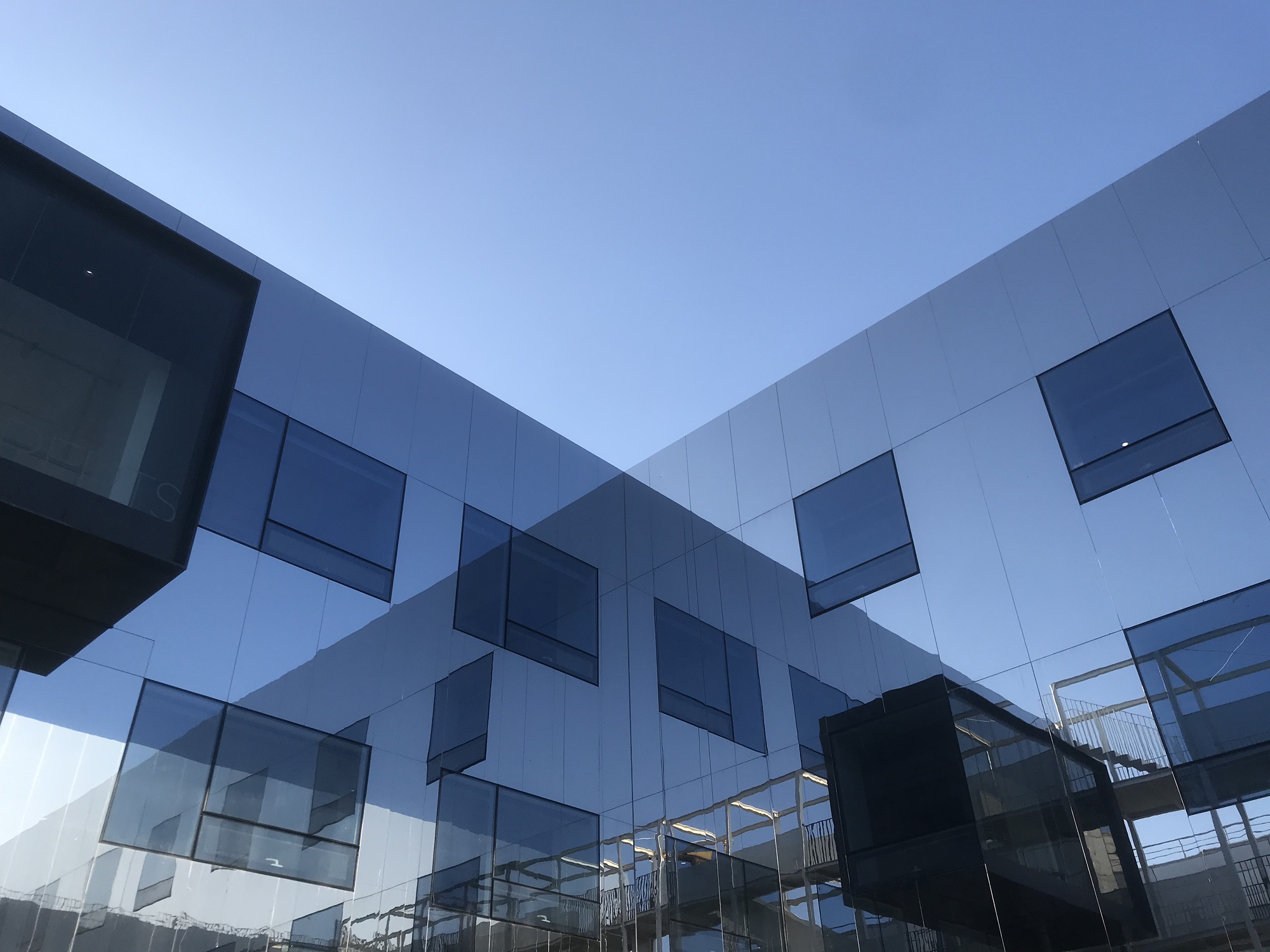Courtyard view showing white and grey panels with irregularly placed protruding windows at dusk