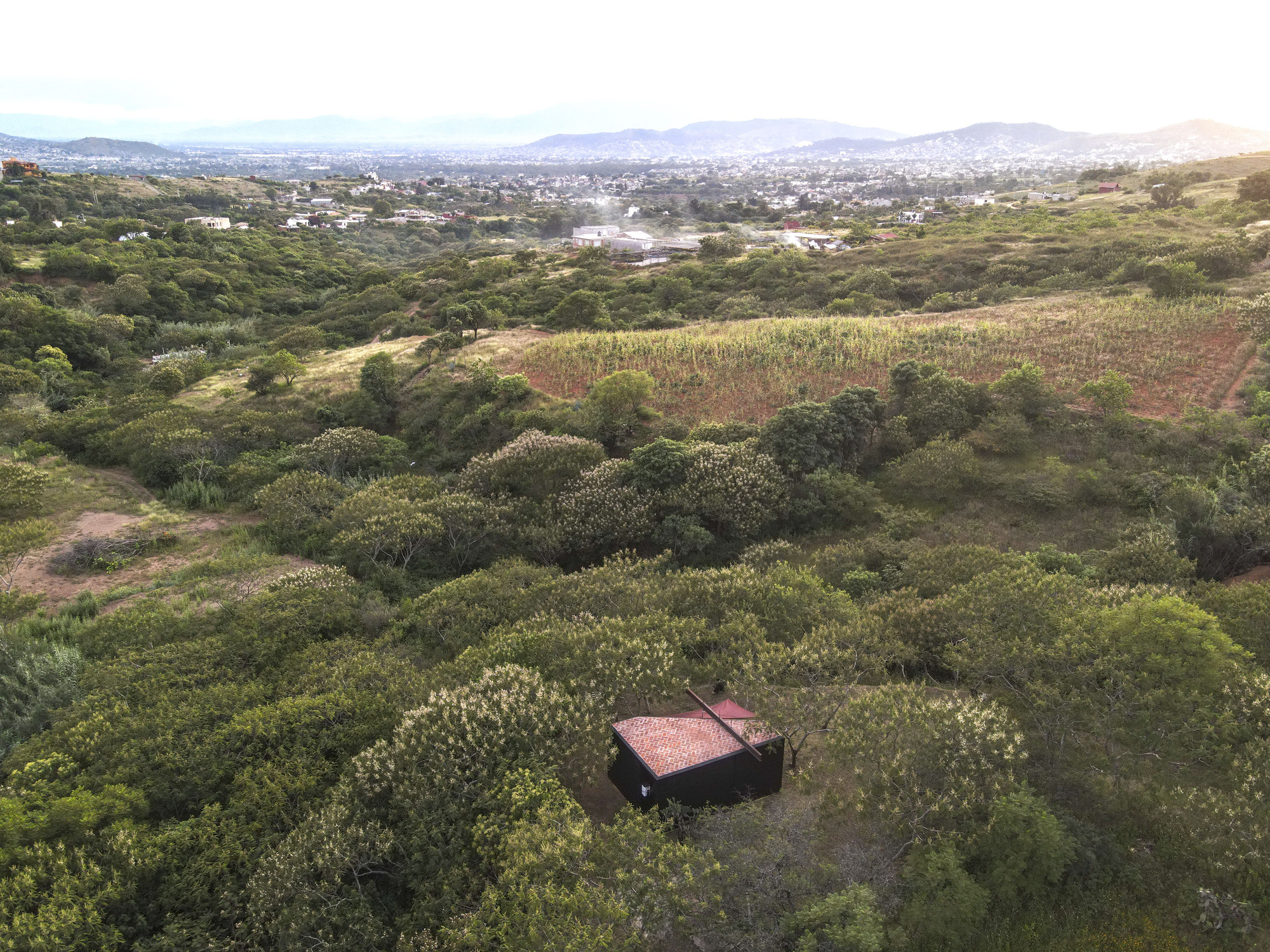 Aerial view of the compact structure with red canopy nestled in dense scrubland vegetation