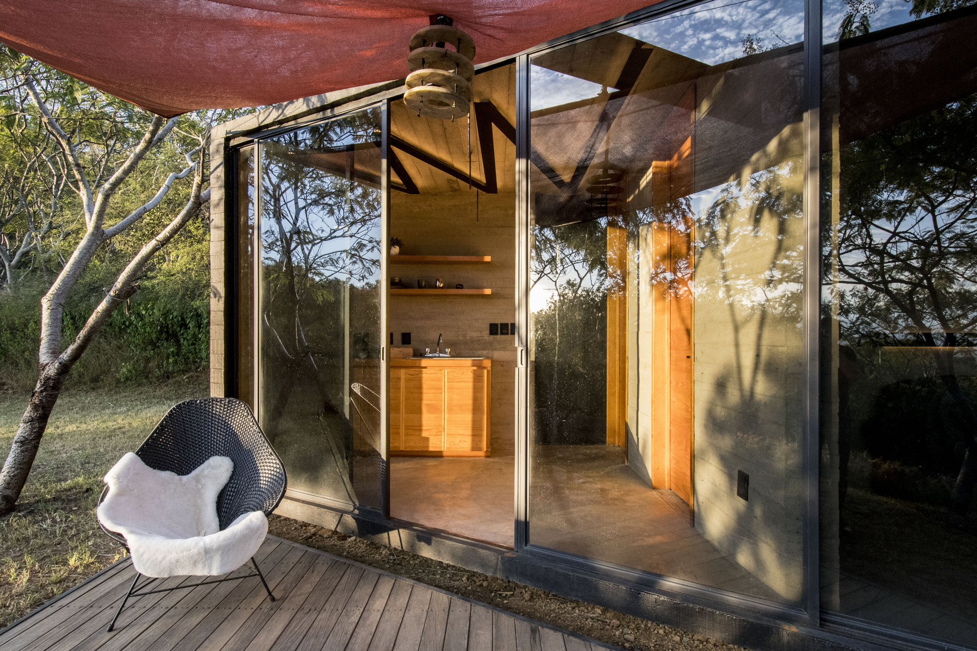 Open glass doors revealing the board-formed concrete interior and spiral stair under dappled afternoon light