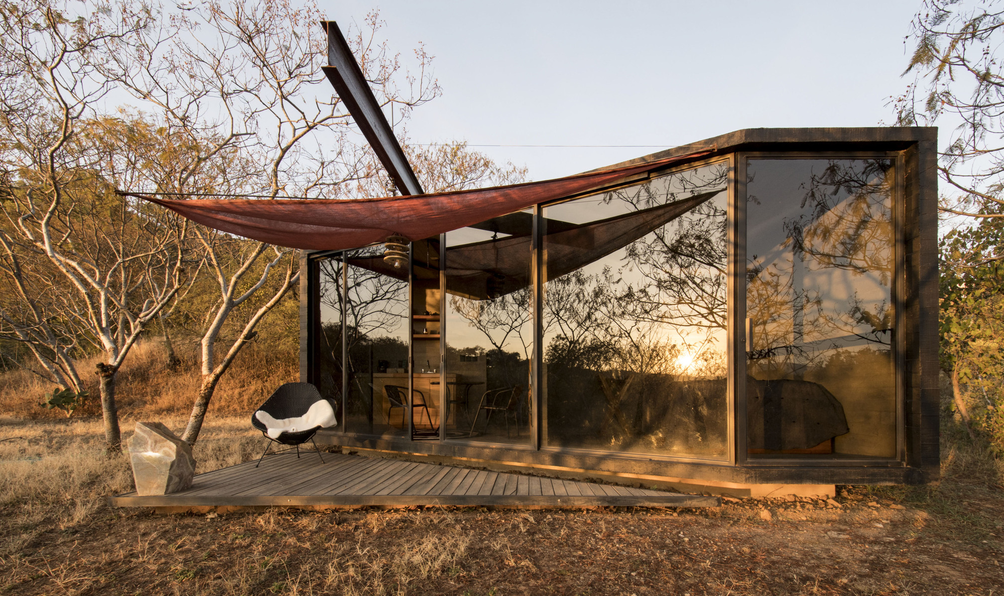 Glazed facade with deck and fabric shade canopy among bare winter trees at dusk