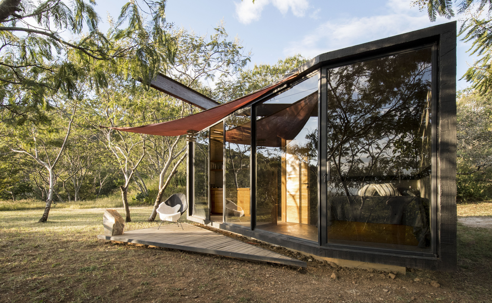 Corner view of the glazed volume with fabric shade canopy suspended above the timber terrace