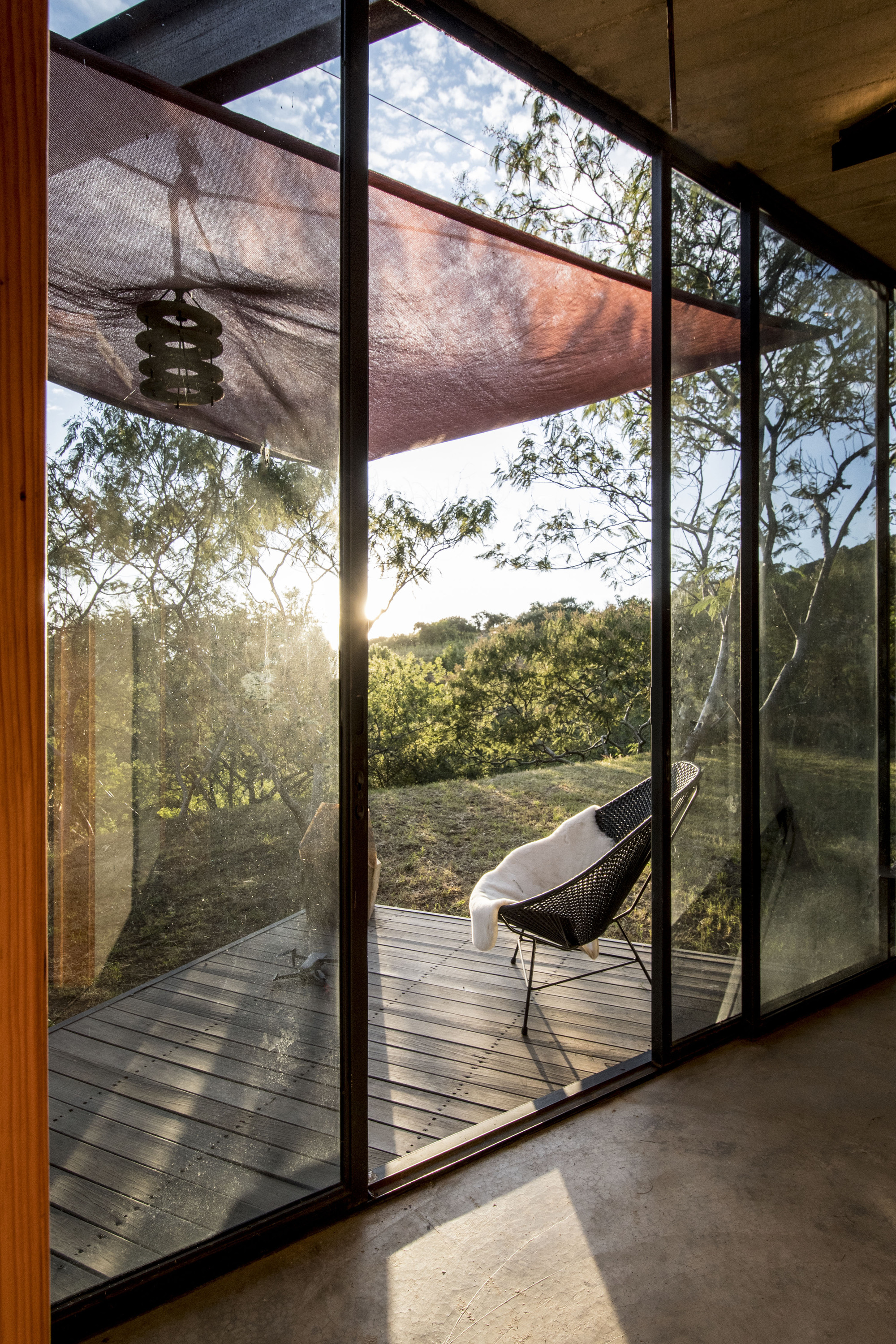 Interior view through floor-to-ceiling glazing to the timber deck and landscape at dusk