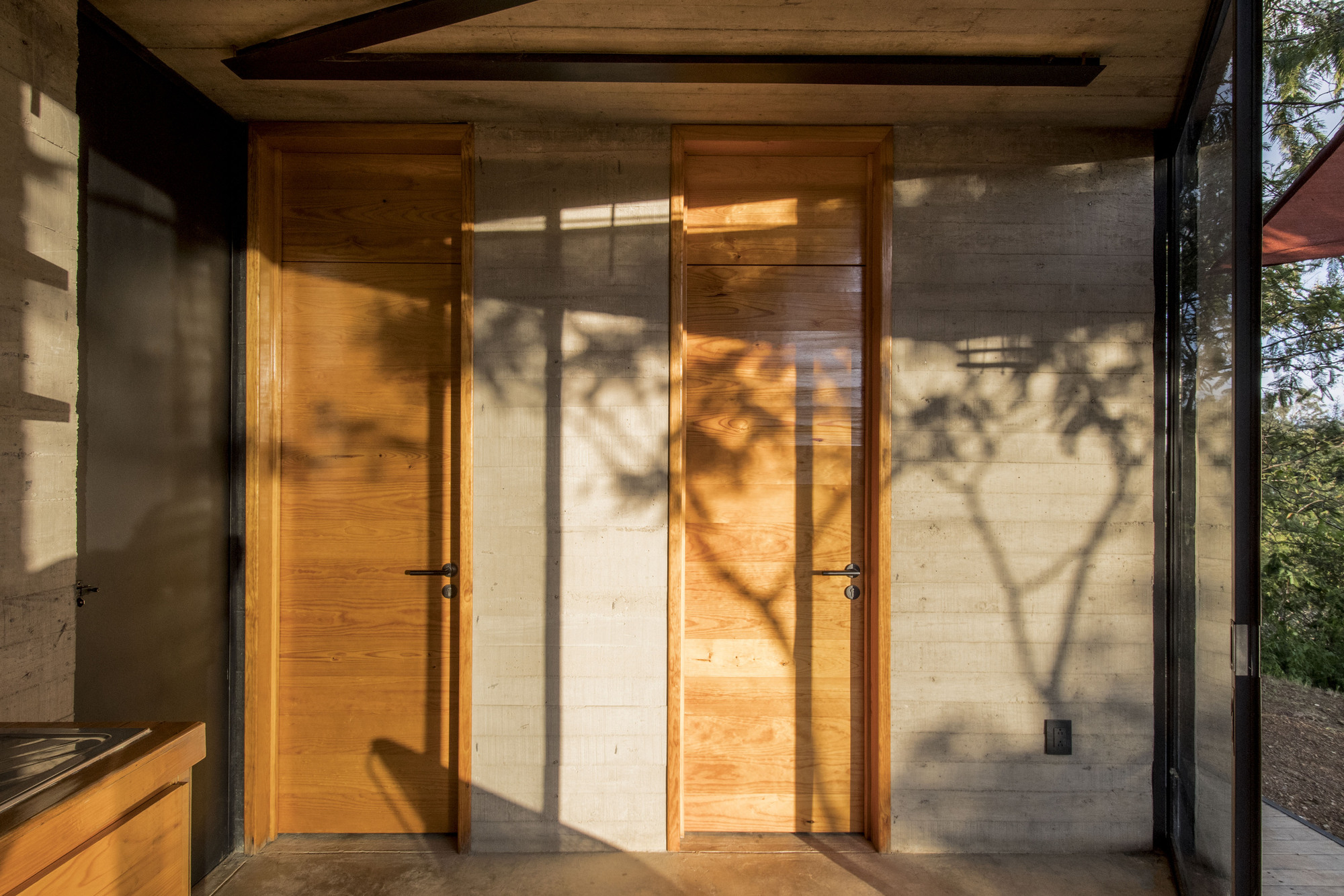 Timber doors in concrete corridor with tree shadows cast across the floor and walls