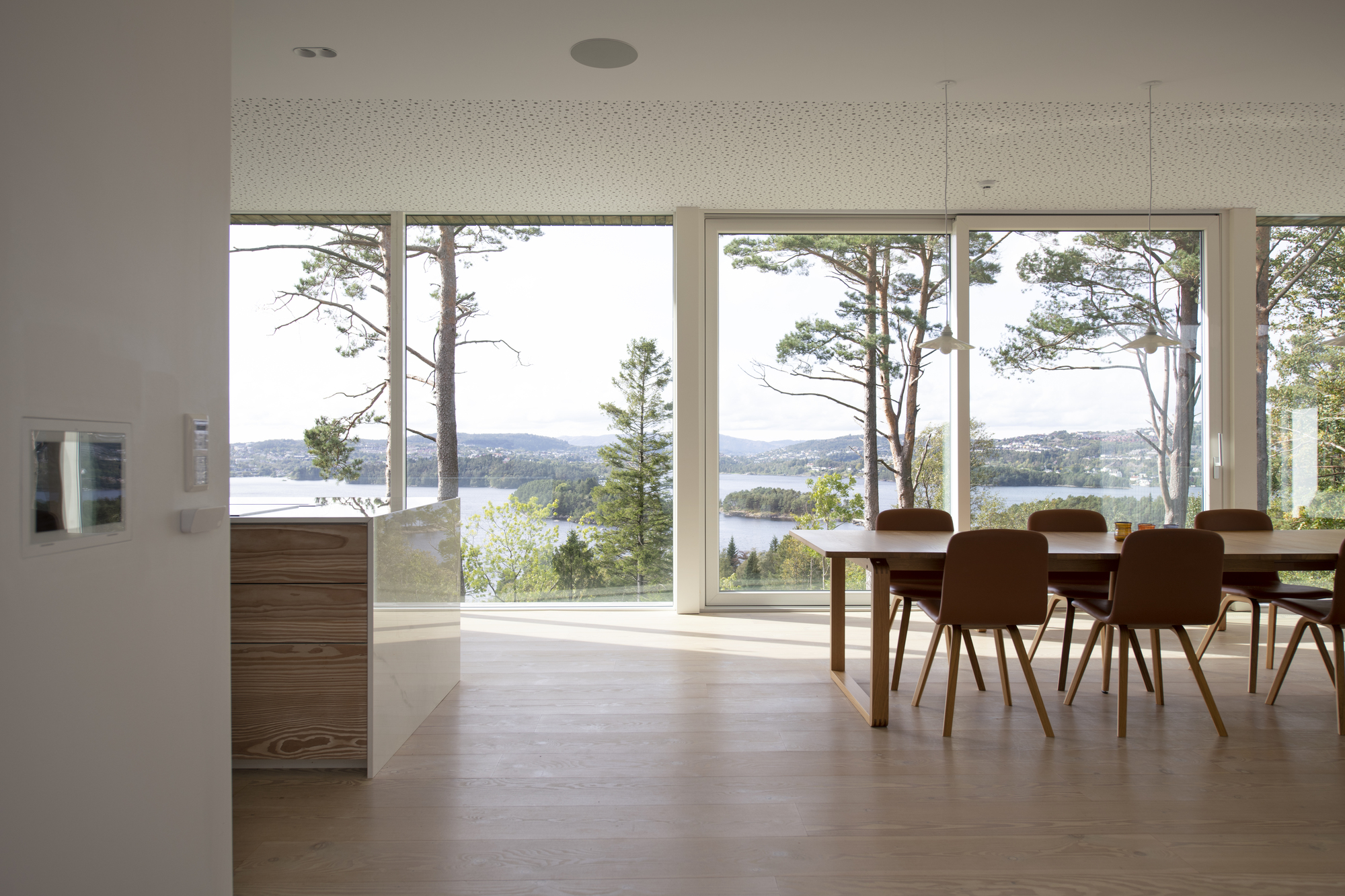 Dining area with floor-to-ceiling windows framing views of water and pines beyond