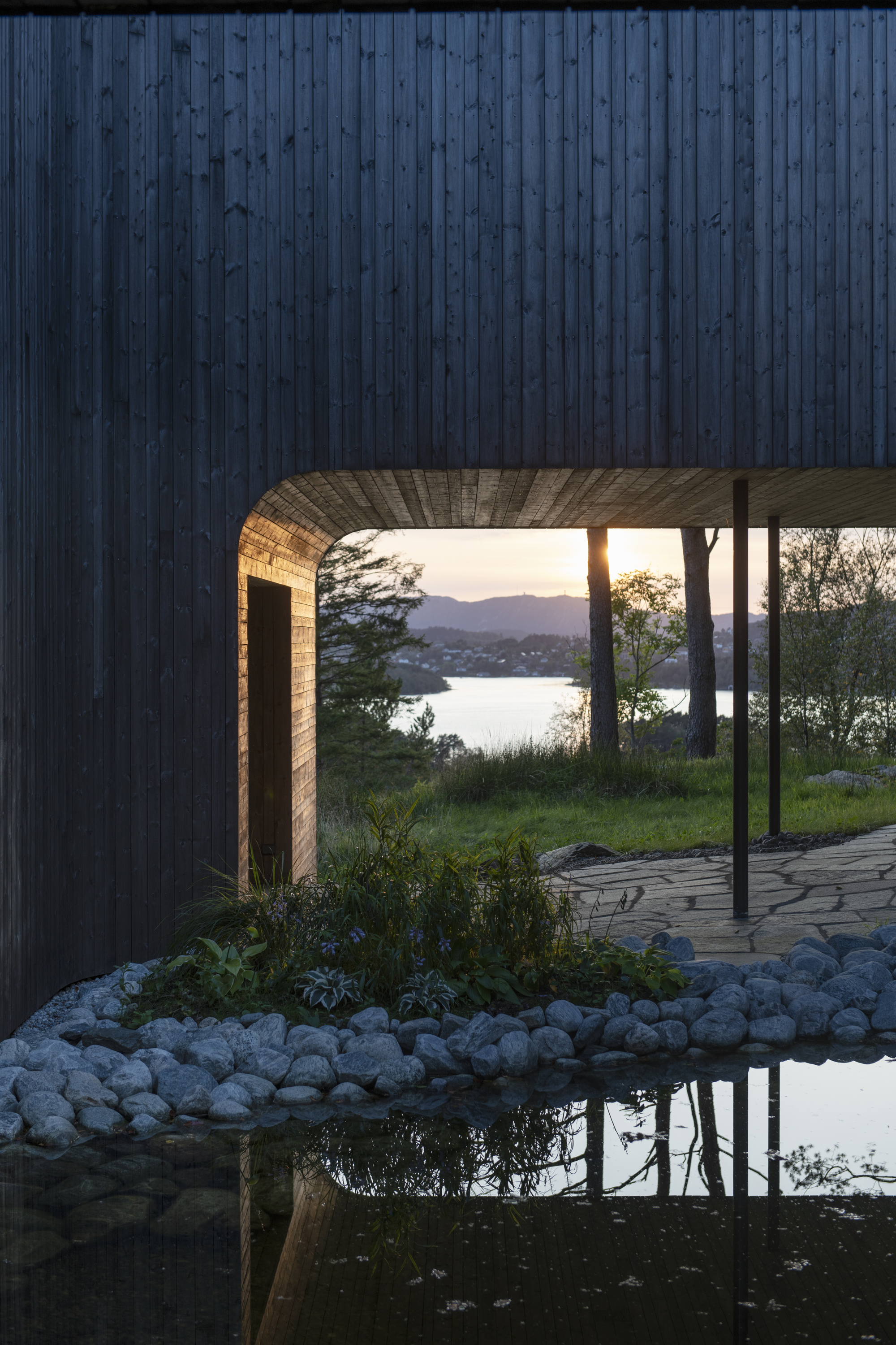 Covered passage with timber-lined soffit framing a view across the water at sunset