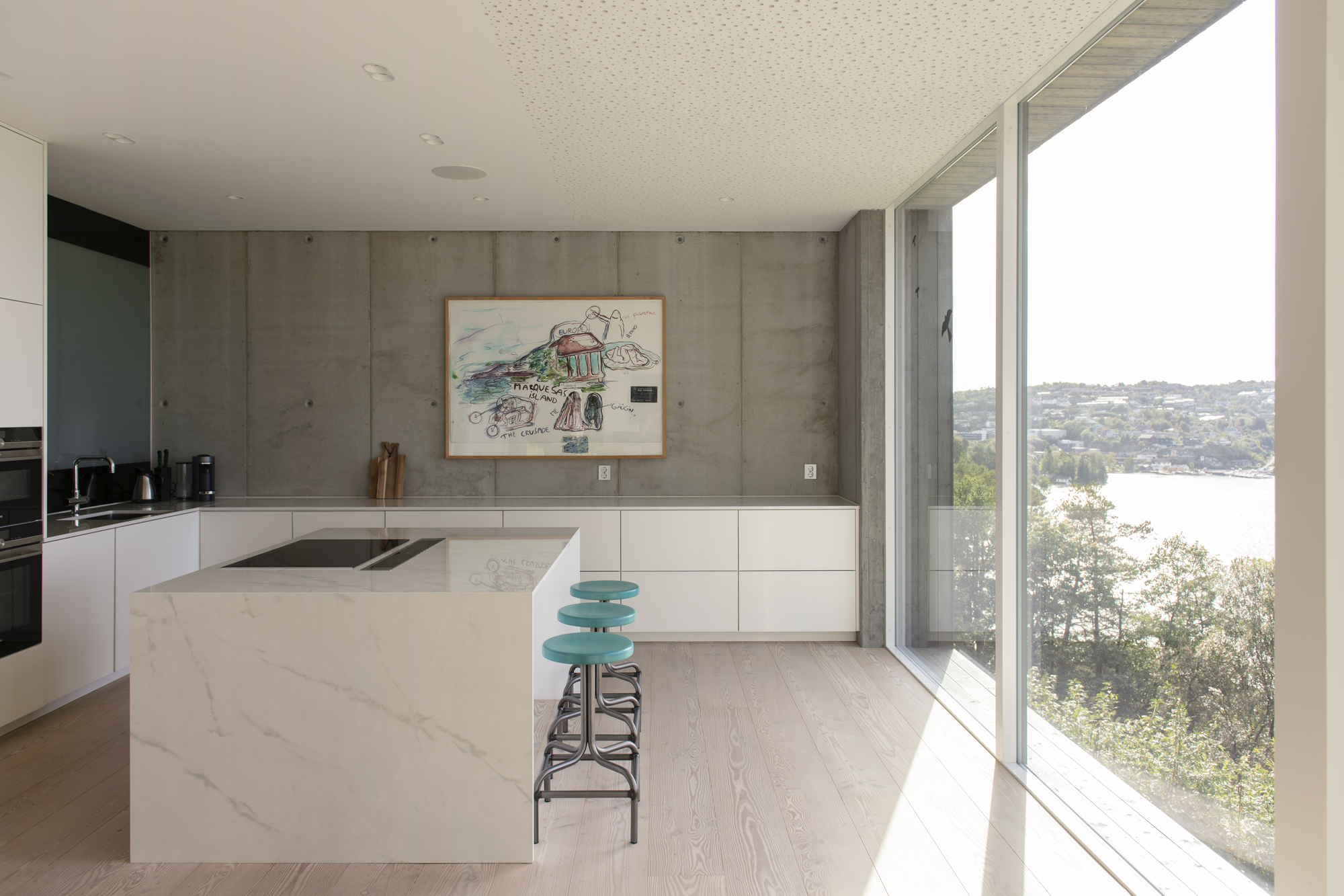 Kitchen with white island and concrete wall opening to water view through glazing