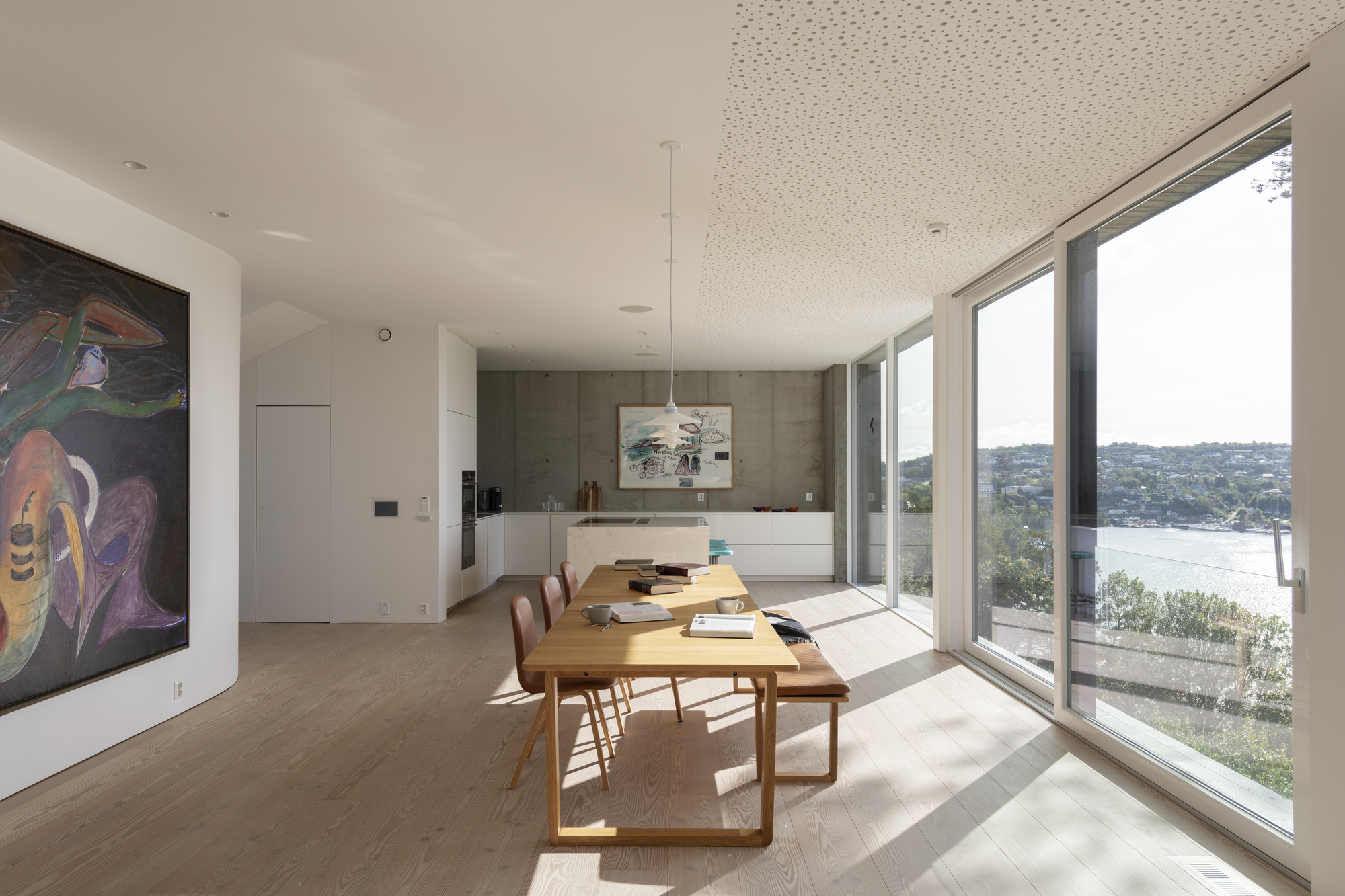 Open dining and kitchen space with timber table and floor-to-ceiling windows overlooking the bay