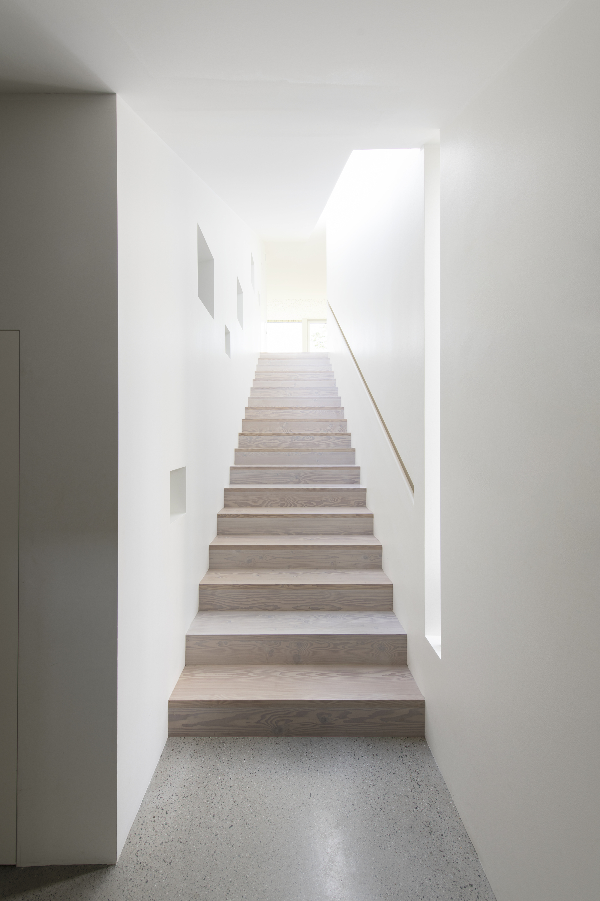 Timber staircase ascending through white walls with skylight above