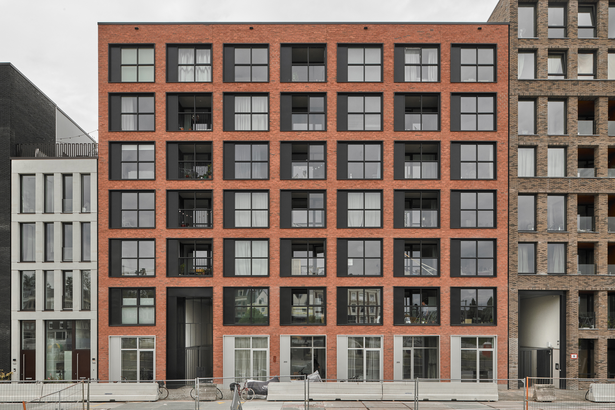 Facade with orange brick grid framing black recessed balconies and gridded windows at ground level
