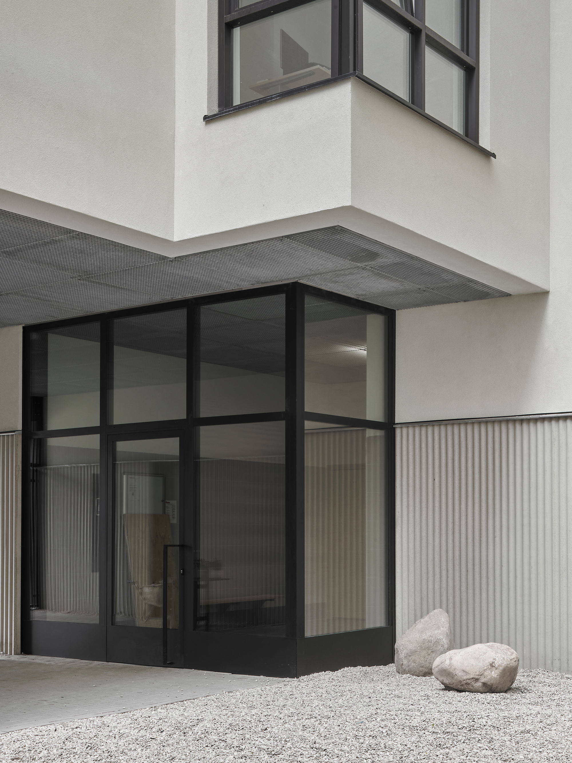 Corner entry detail showing black-framed glass doors, vertical corrugated cladding, and overhanging volume above