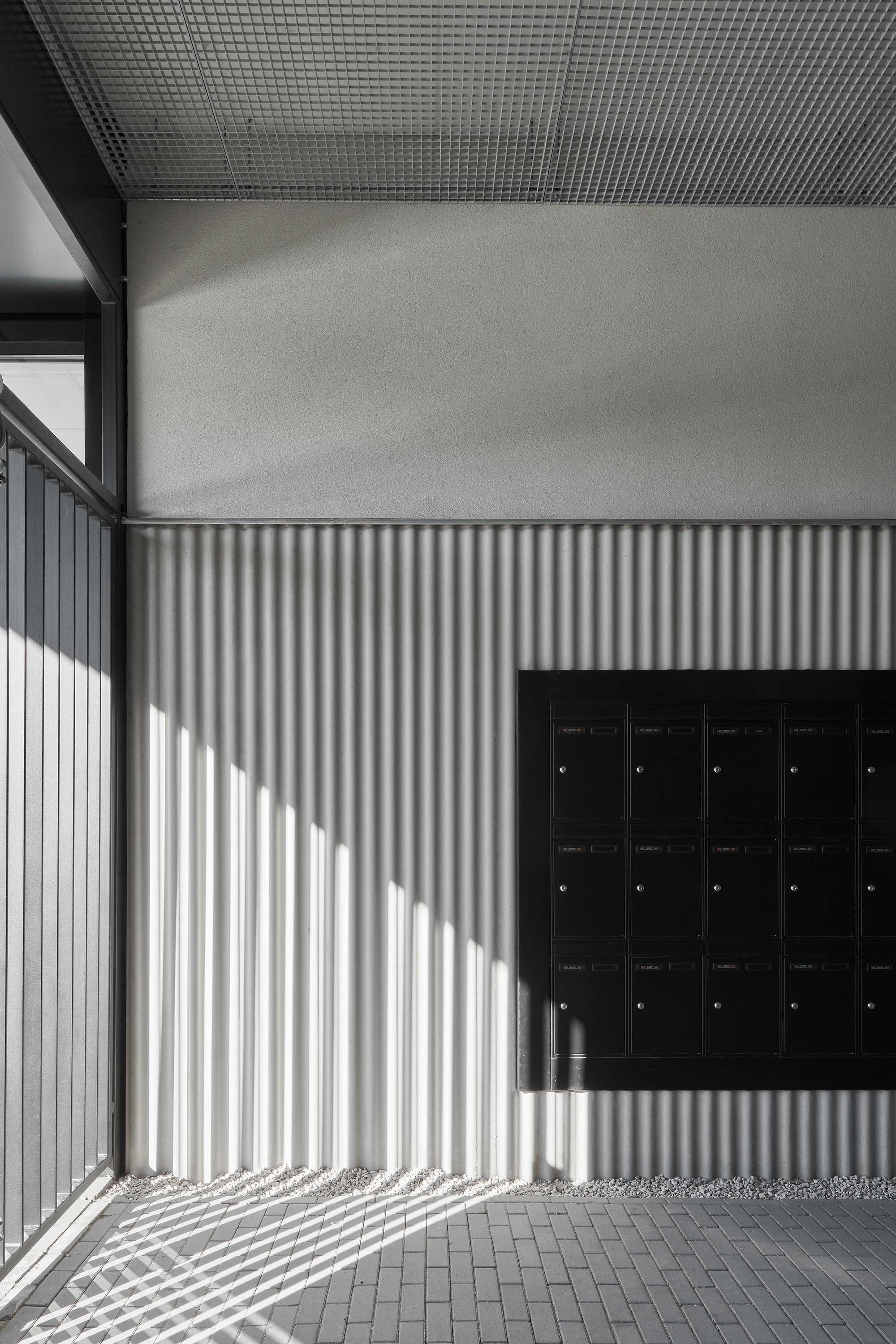 Entry alcove with corrugated metal wall casting striped shadows beside a black mailbox bank