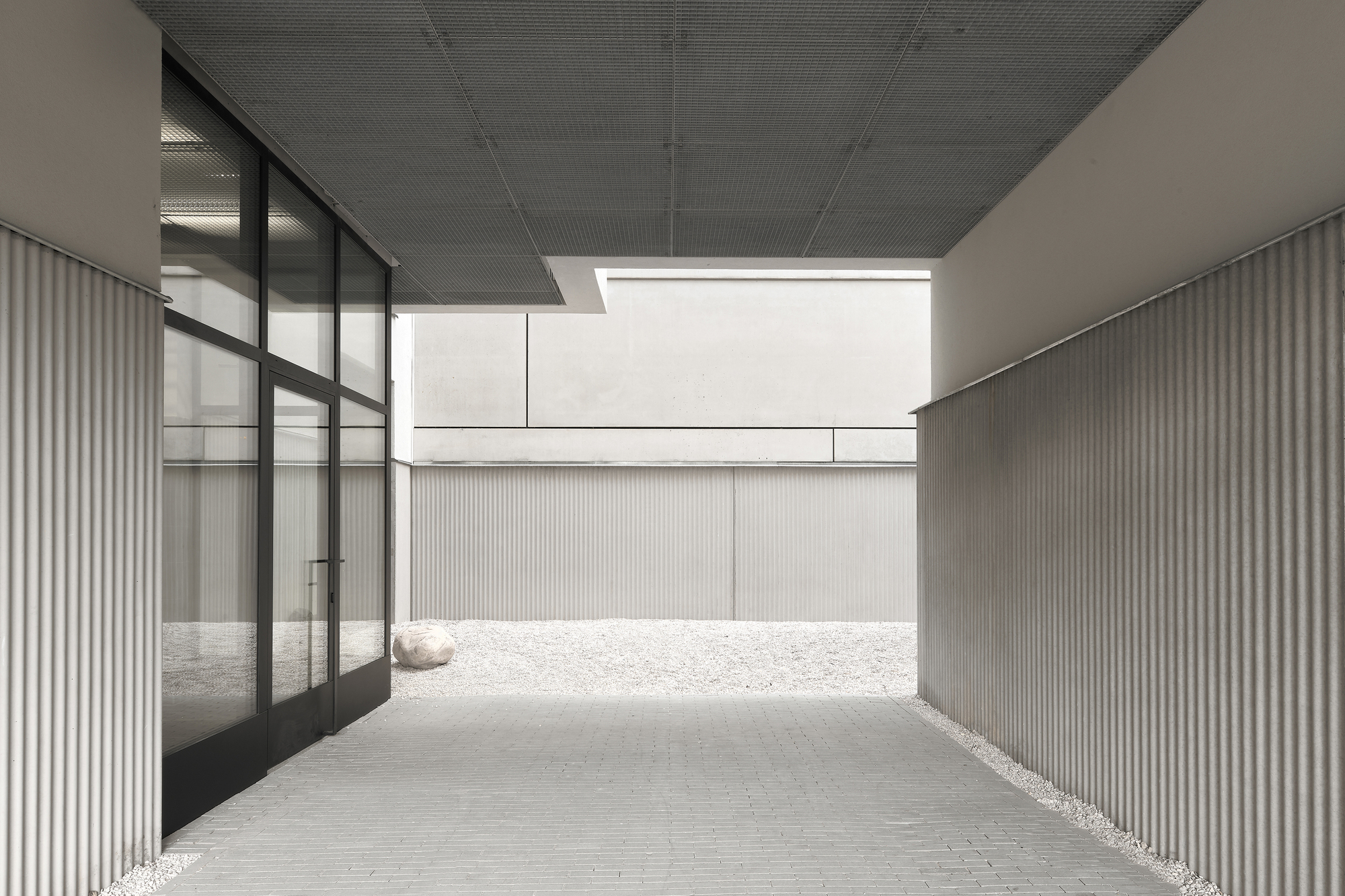 Covered passage with ribbed ceiling and glass wall opening to a gravel courtyard beyond