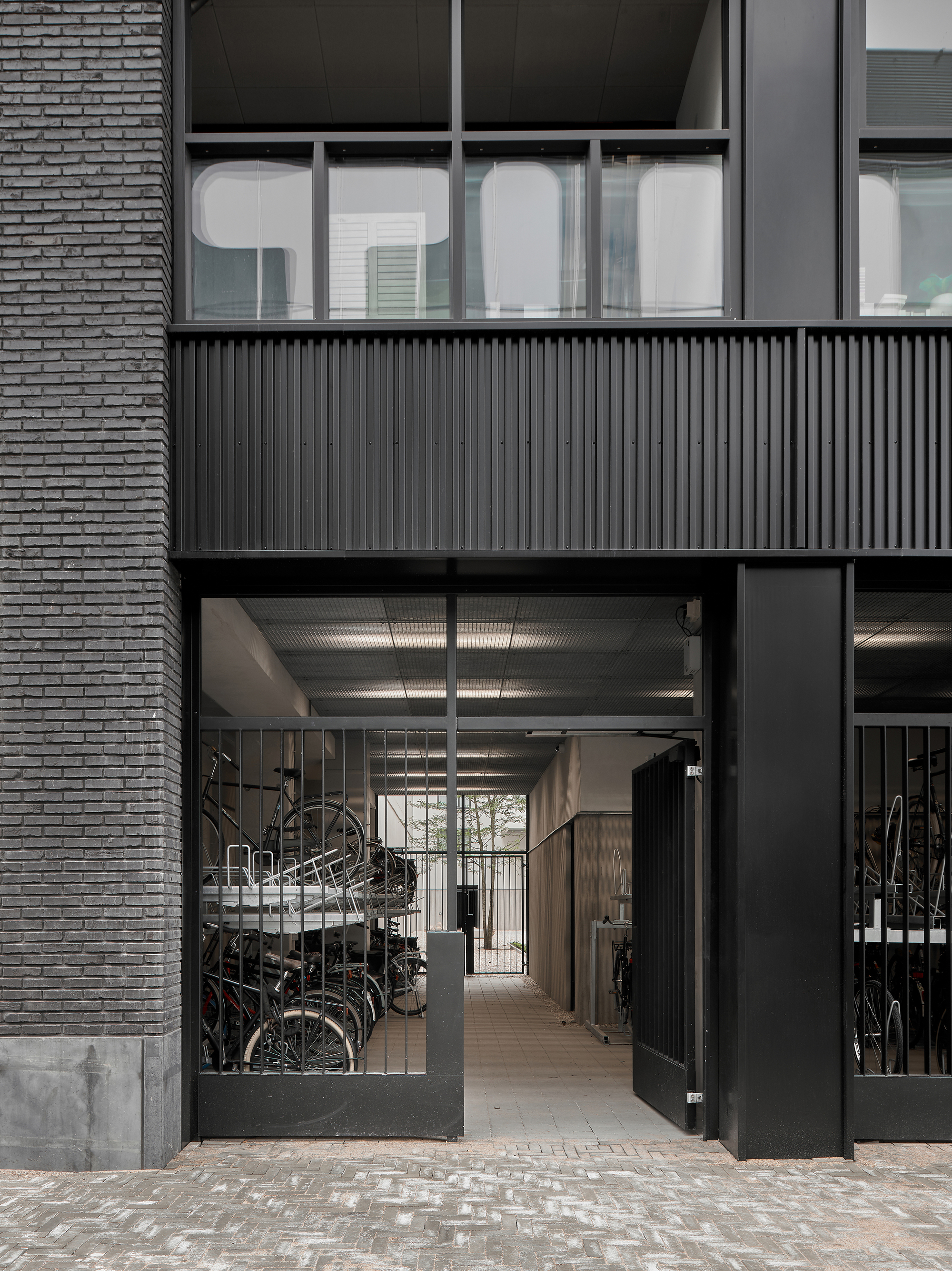 Ground-floor entrance with glazed doors opening to bicycle storage beneath corrugated metal ceiling