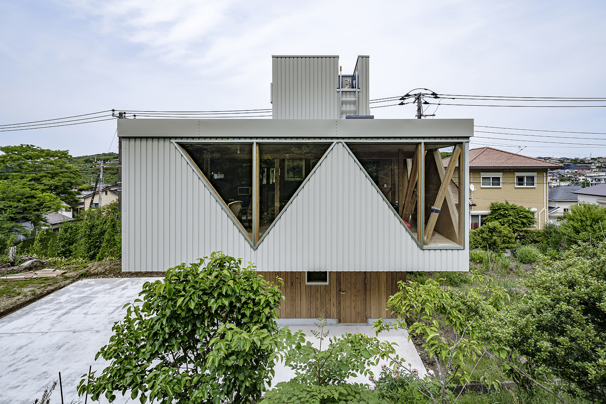 Triangular cutout windows in the corrugated metal facade framing exposed timber diagonal bracing