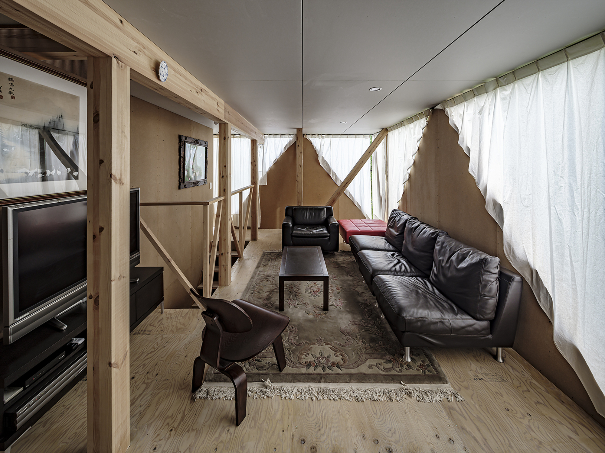 Living room with exposed timber framing, diagonal braces, white curtains and polished concrete floor