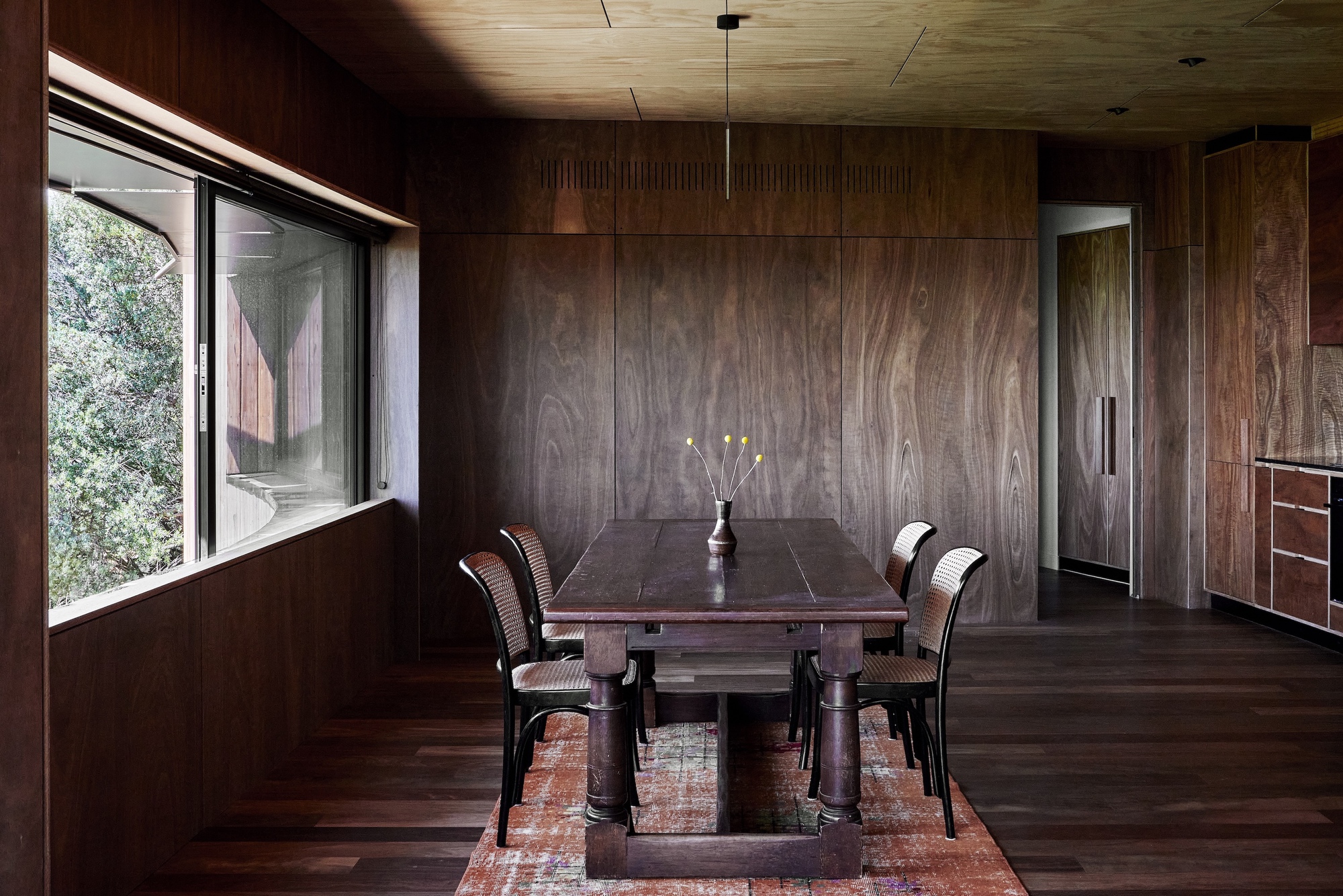 Dining room with dark wood-paneled walls and ceiling lit by a linear fixture