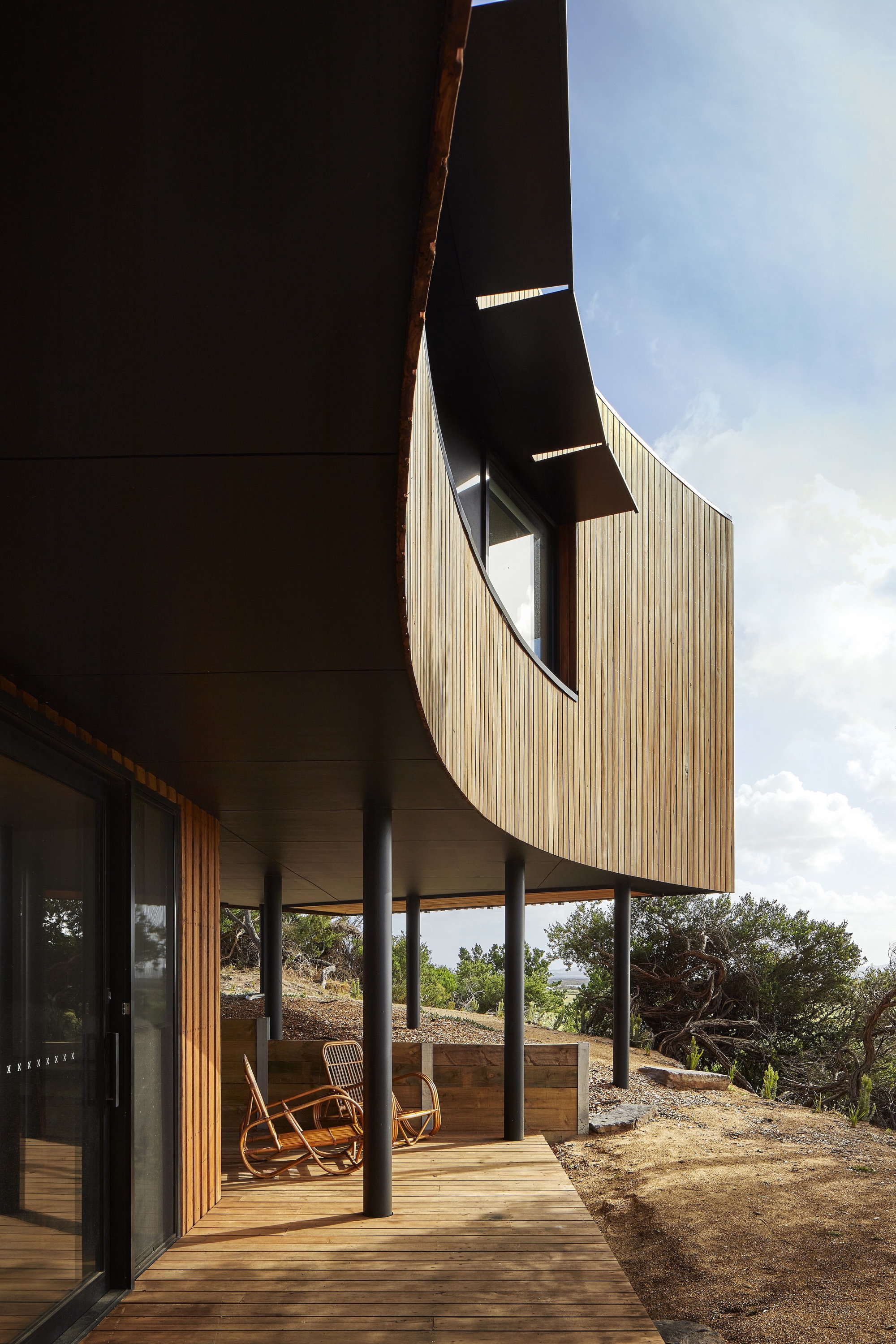 Covered timber deck beneath the cantilevered upper floor with rocking chairs looking toward the hills