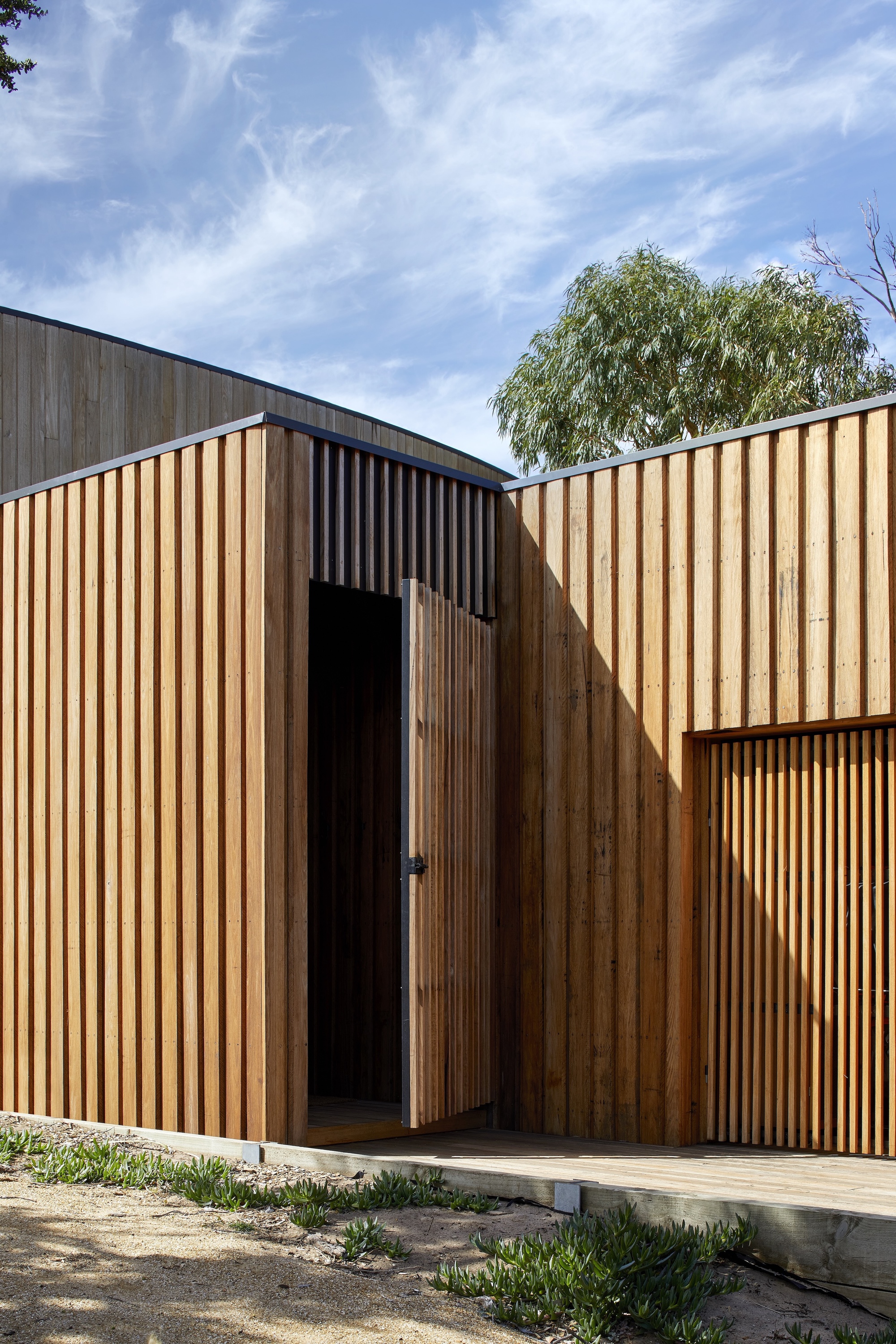 Vertical timber screen facade with recessed entry portal beneath a willow tree